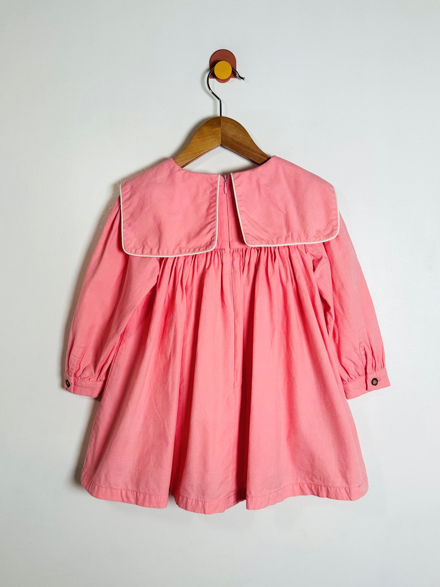 Pink dress on a wooden hanger against a white background