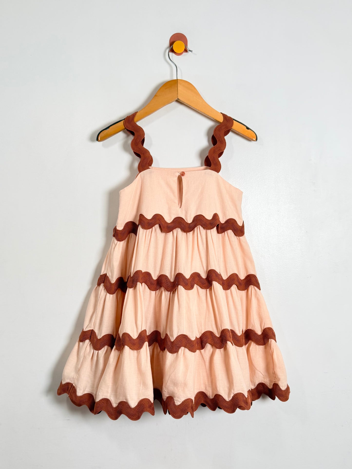 Beige dress with brown ruffled trim on a hanger against a white background