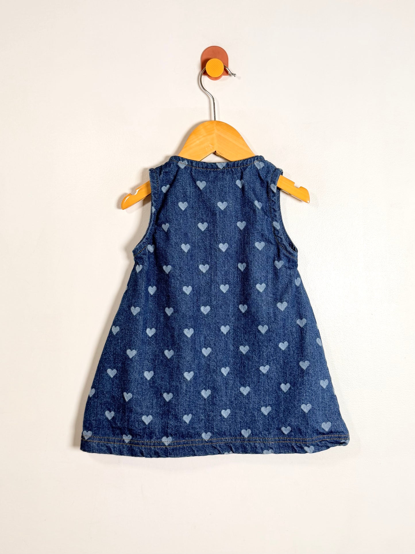 Blue denim dress with heart patterns on a wooden hanger against a white background