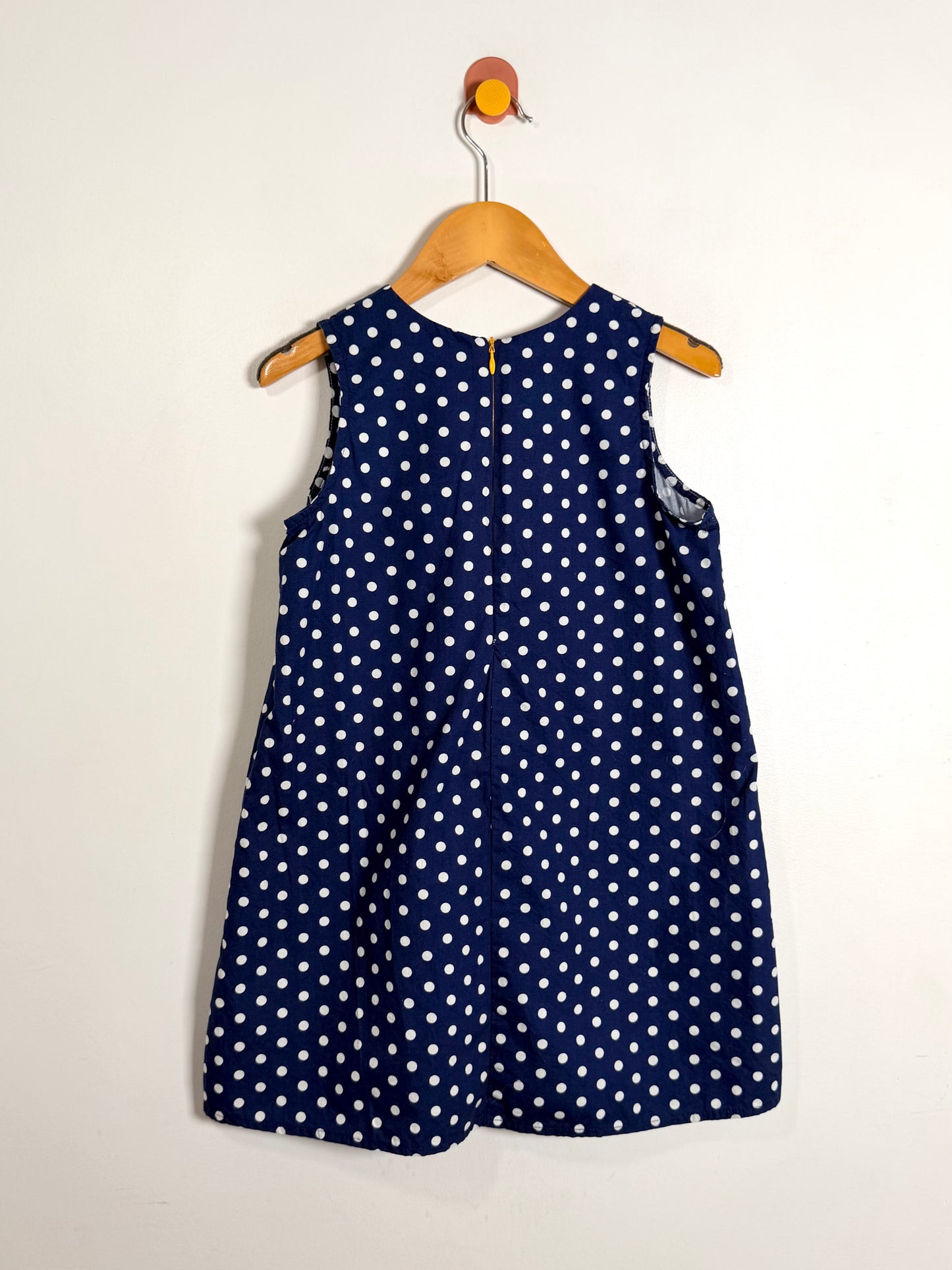 Navy blue dress with white polka dots on a wooden hanger against a white background