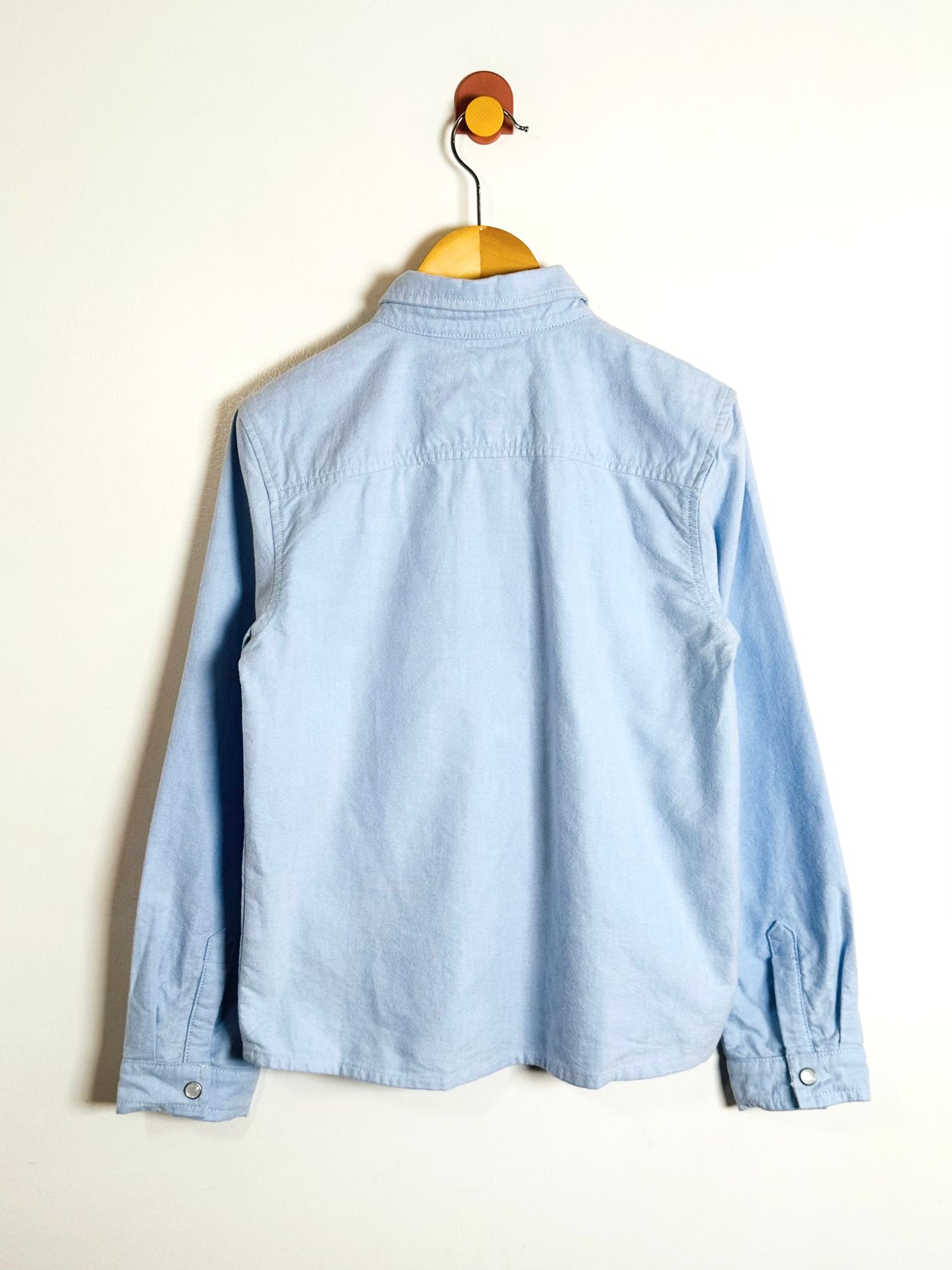 Light blue denim shirt on a hanger against a white background