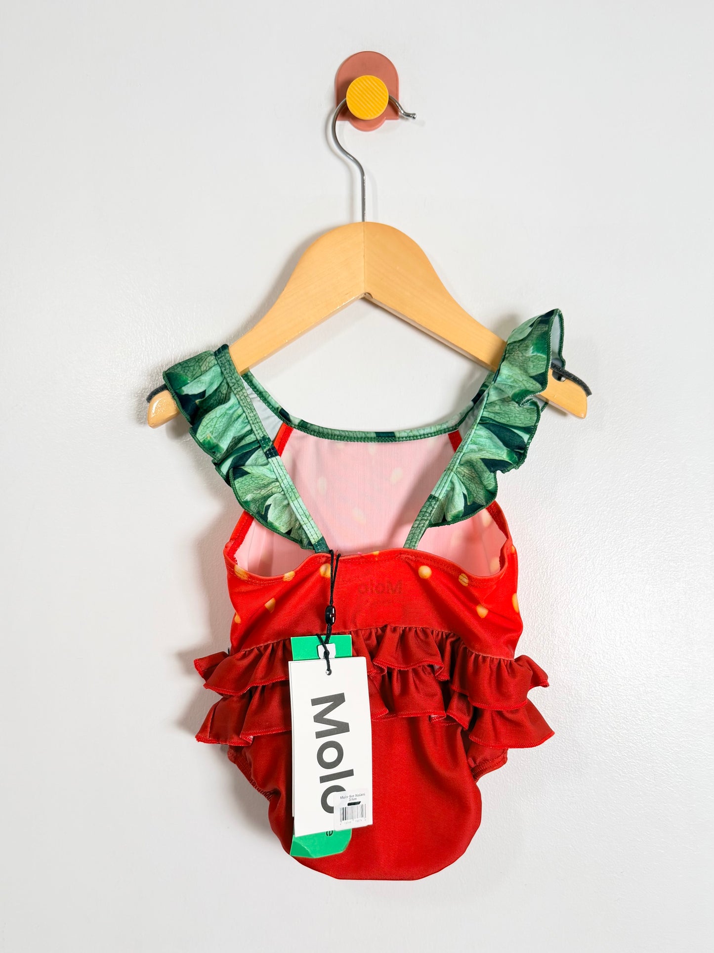 Red and green children's swimsuit on a hanger with a visible brand tag.