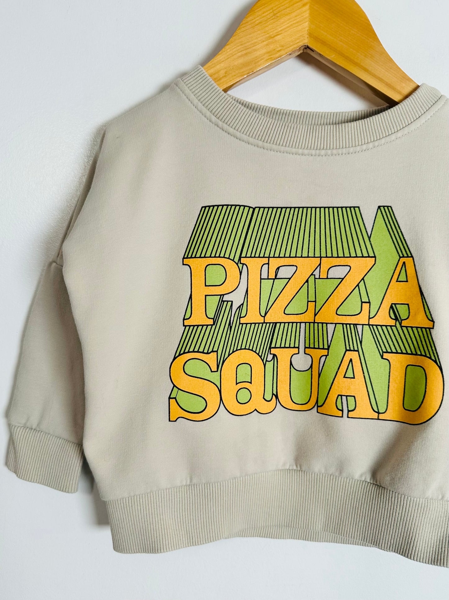 Beige sweatshirt with 'Pizza Squad' text on a hanger against a white background