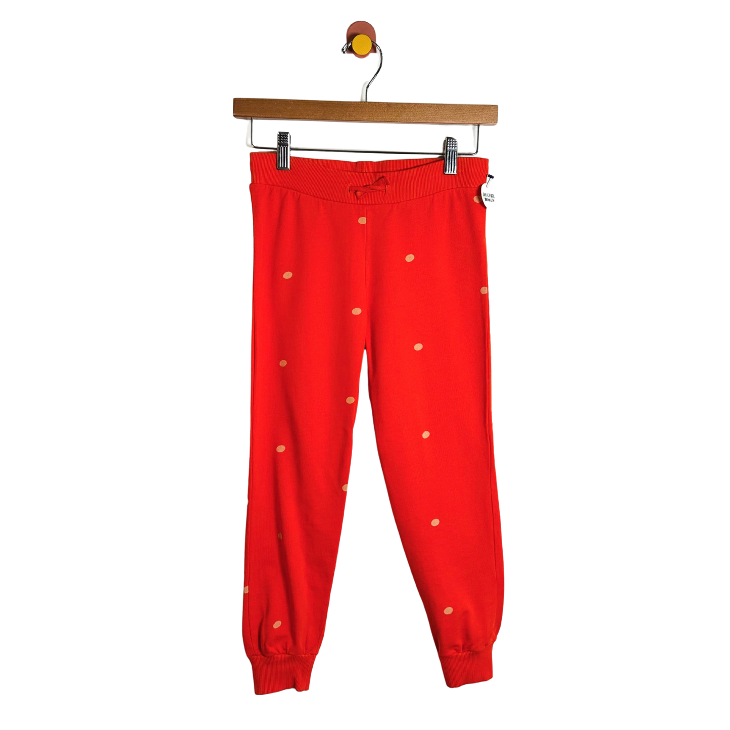 Red pants with white polka dots hanging on a wooden hanger against a white background