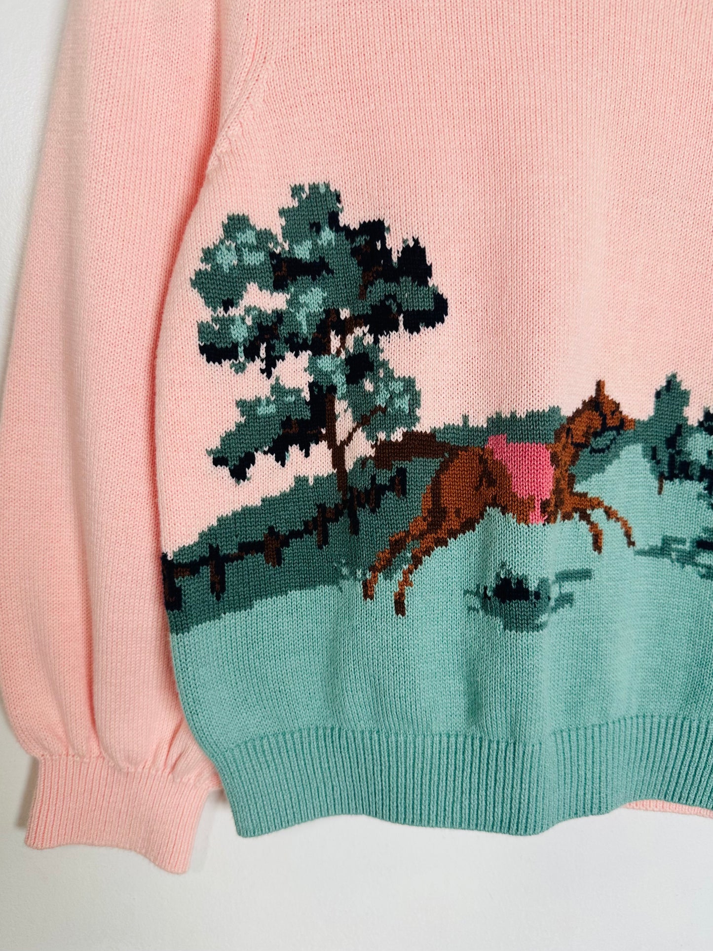 Pink sweater with a horse and tree design on a white background