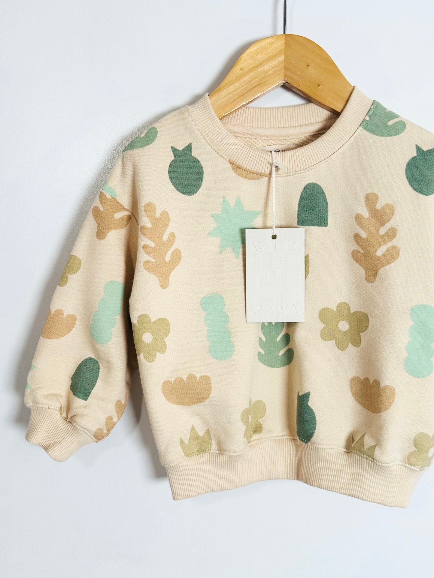Children's sweater with leaf patterns on a hanger against a white background