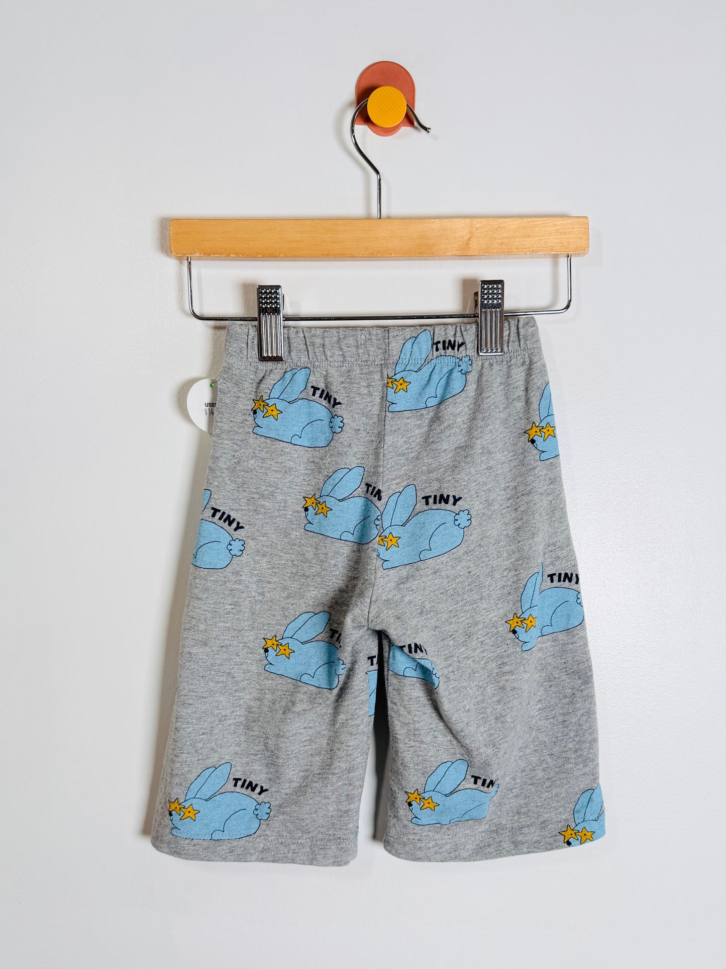 Gray heathered children's shorts with a light blue bunny print and small yellow accents, hanging from a wooden hanger against a plain light background.