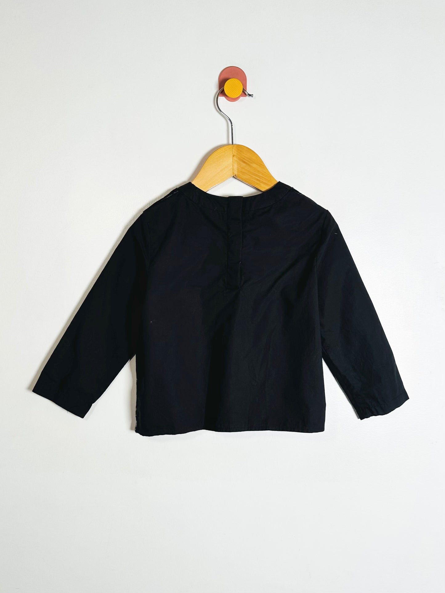 Black long-sleeve shirt on a wooden hanger against a white background