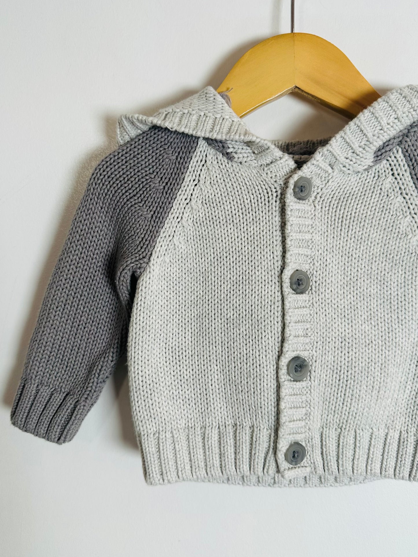 Gray knitted cardigan with button details on a wooden hanger against a white background