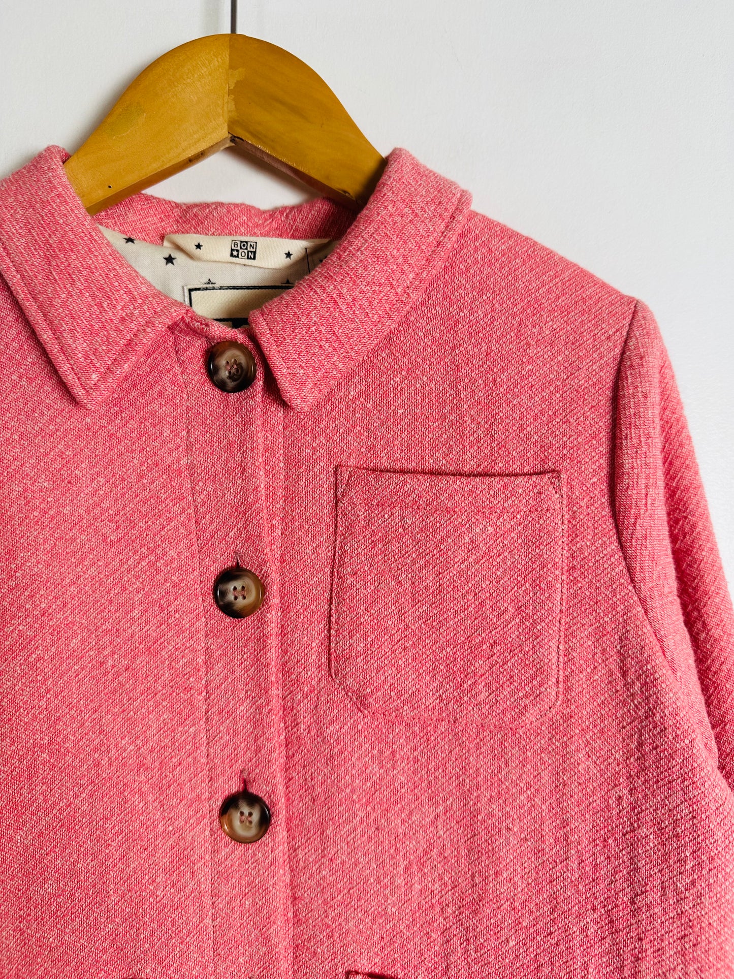 Pink textured jacket with buttons on a wooden hanger against a white background