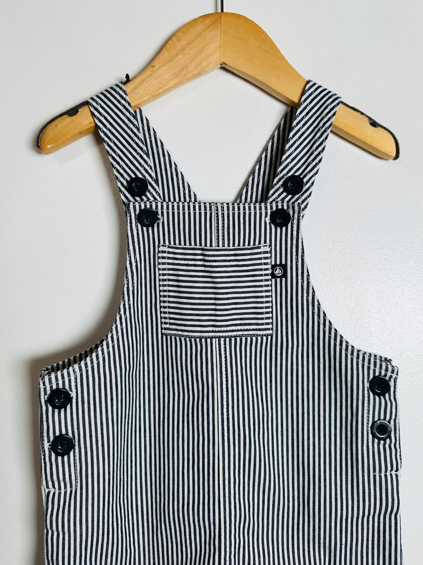 Black and white striped overalls with buttons on a wooden hanger against a white background