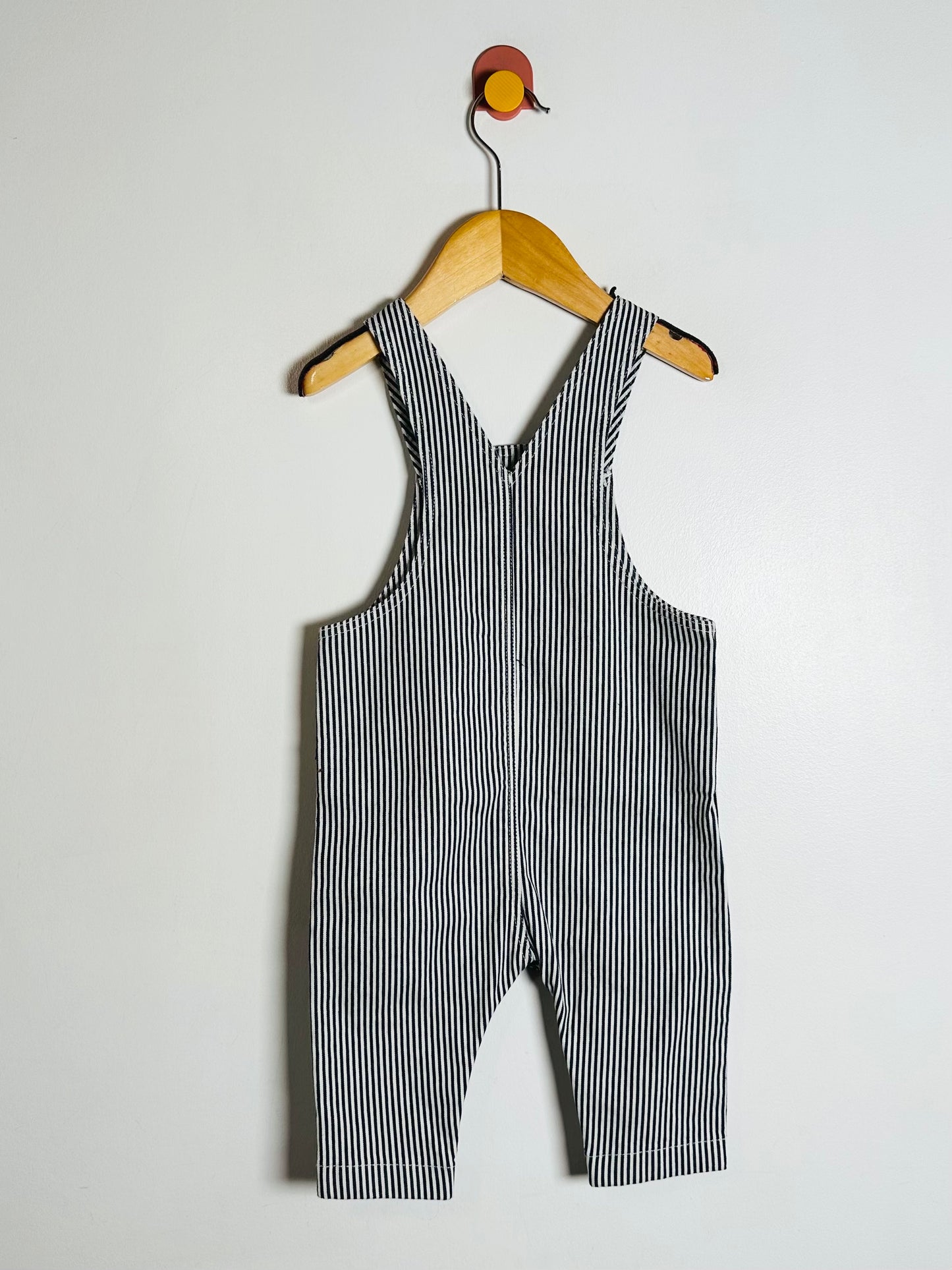 Black and white striped overalls hanging on a wooden hanger against a plain background