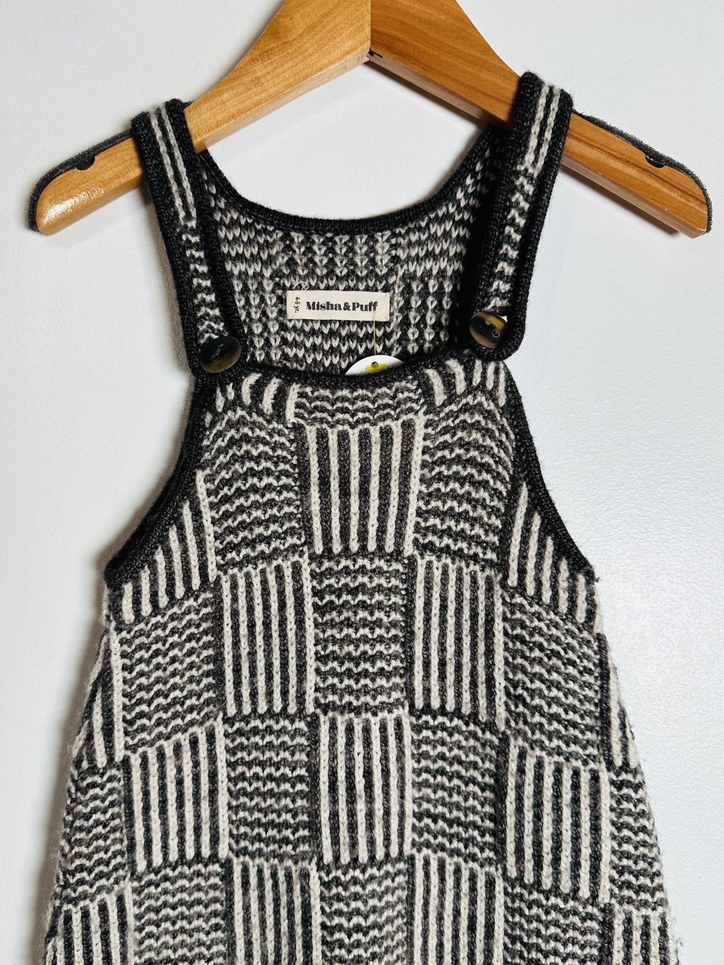 Black and white checkered dress with button details on a wooden hanger against a light background
