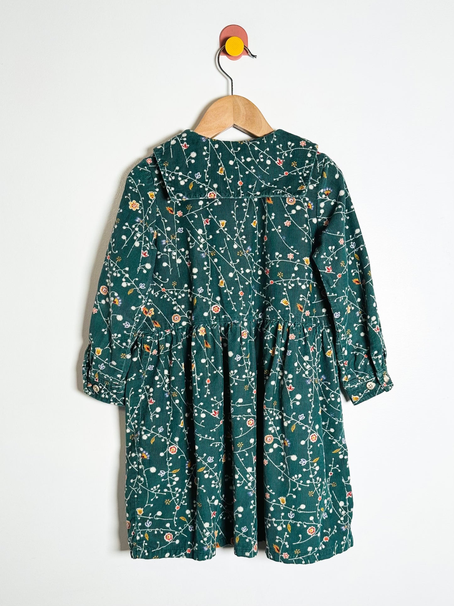Green floral dress on a hanger against a white background