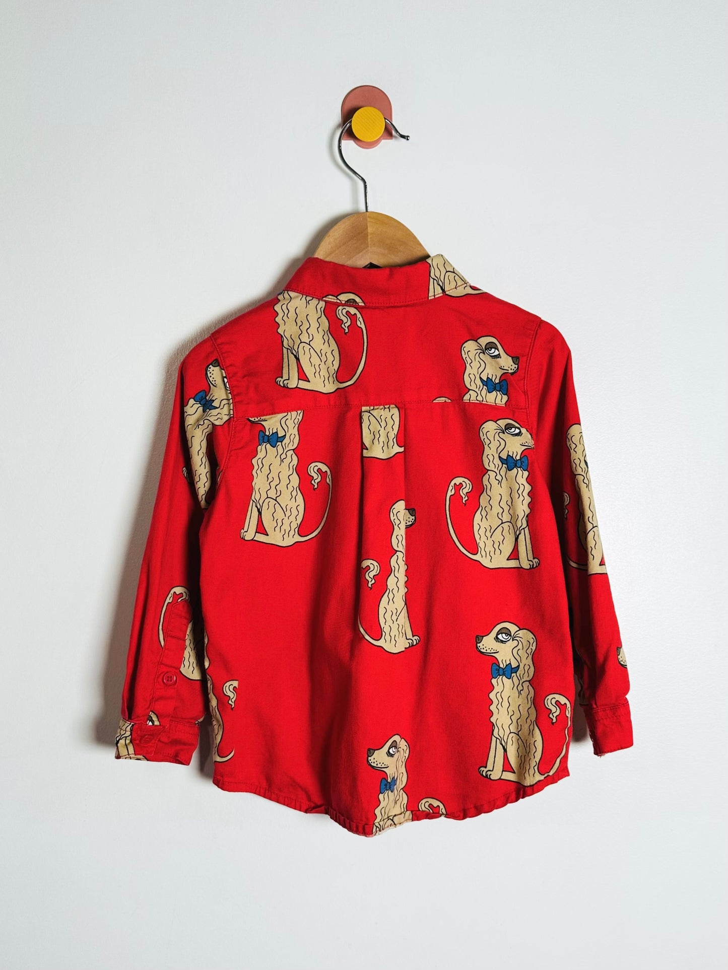 Red shirt with dog pattern on a wooden hanger against a white background