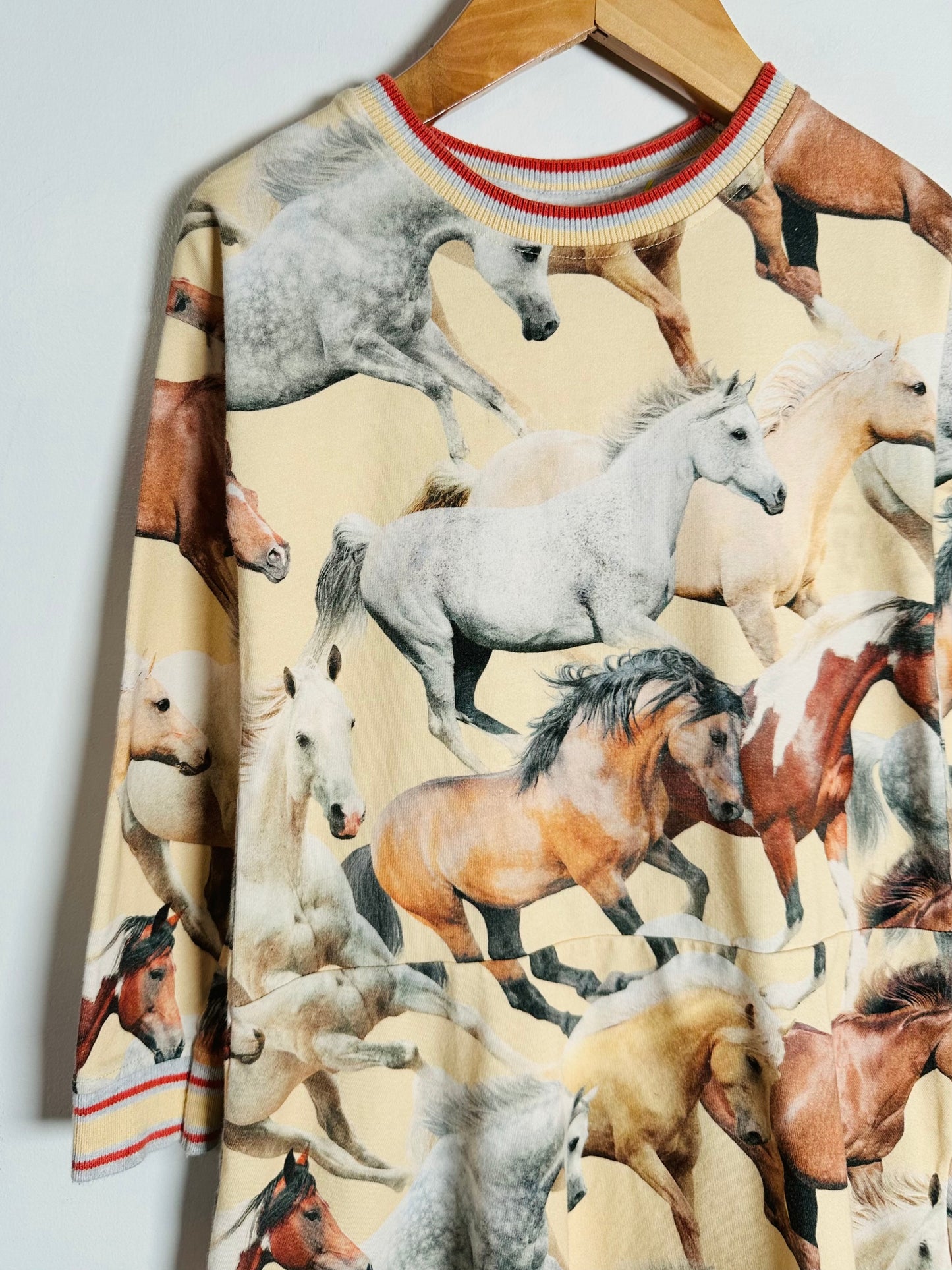 Children's dress with horse pattern on a hanger against a white background