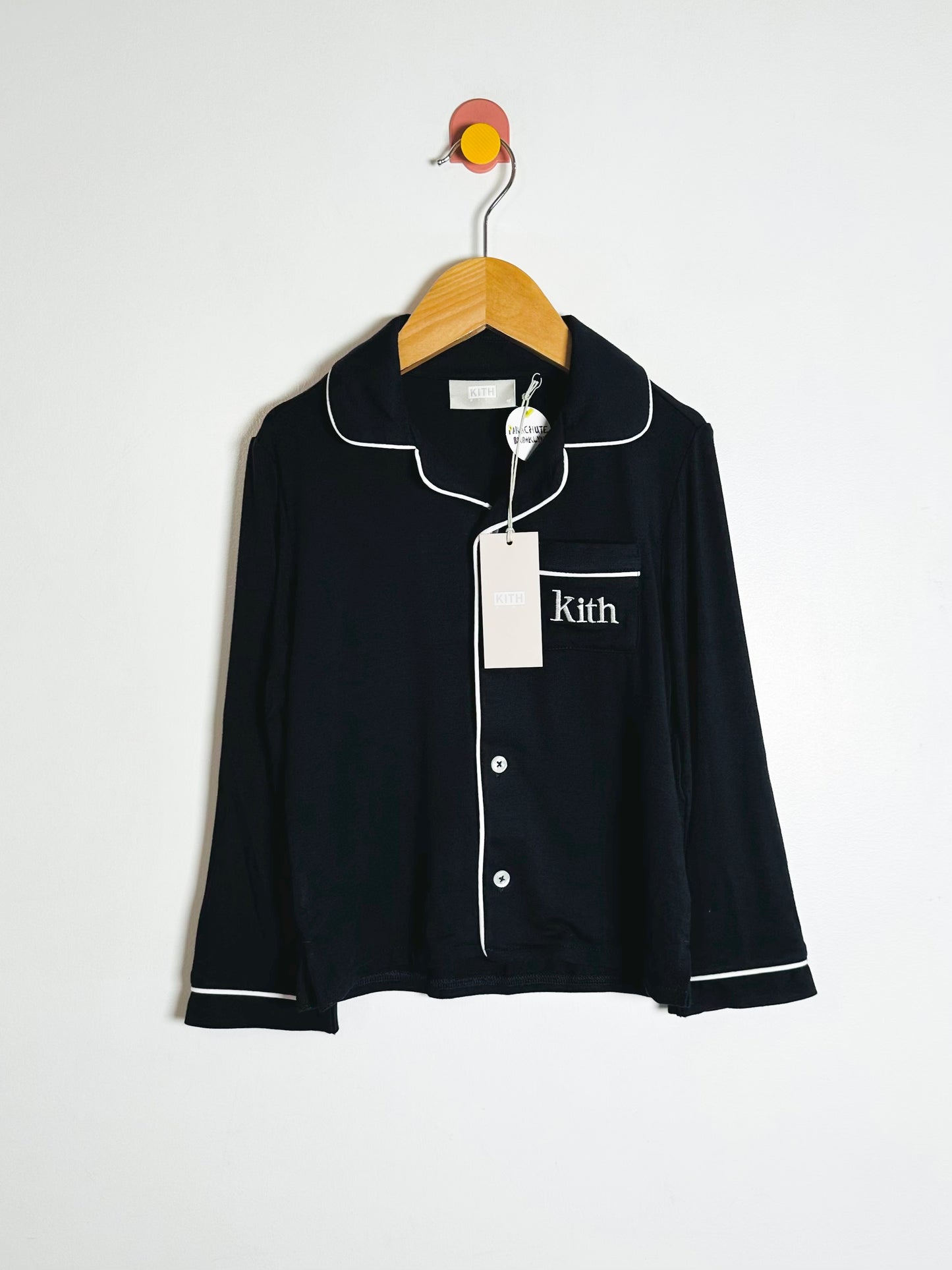 Black pajama top with white piping on a hanger against a white background