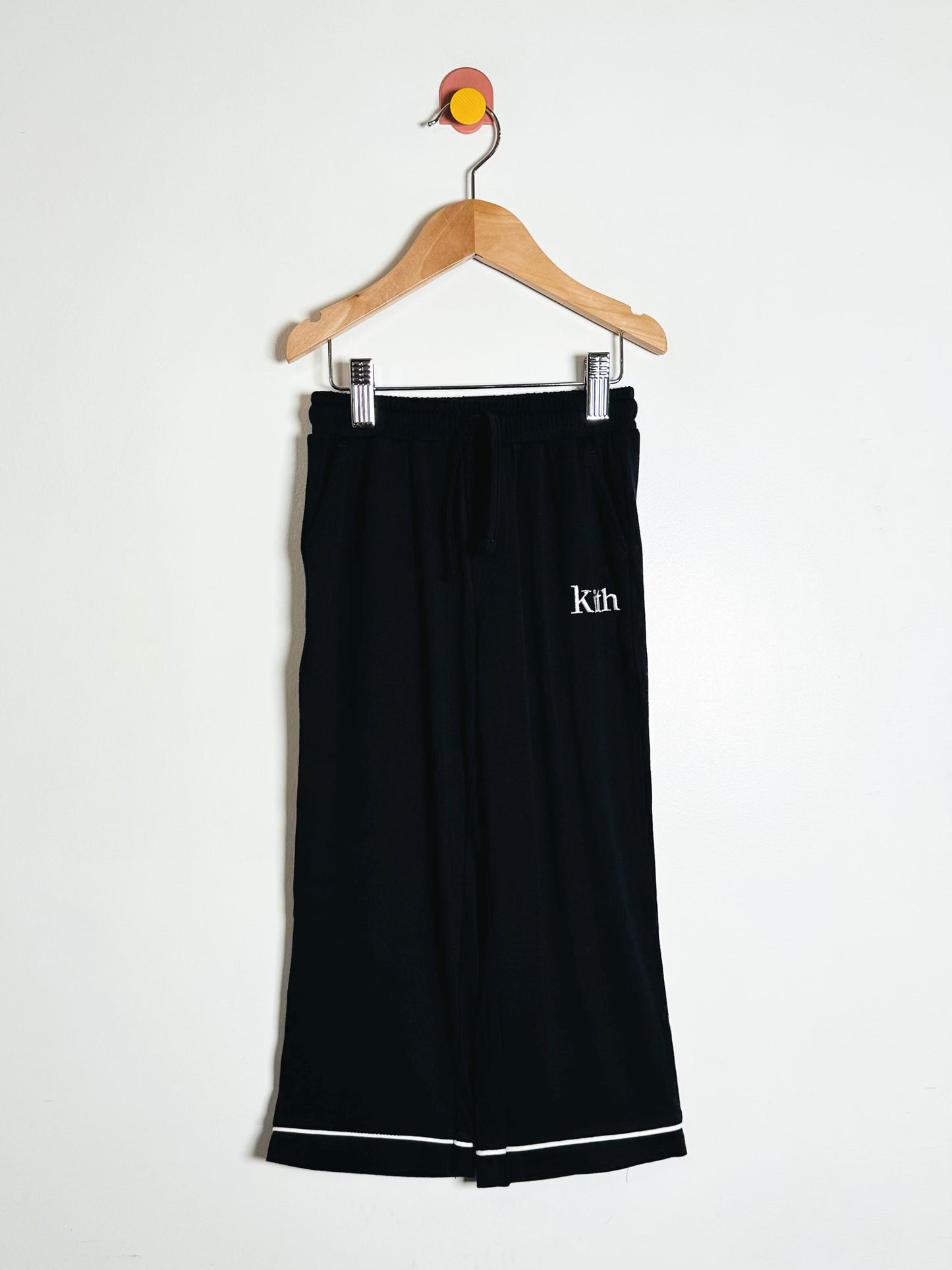 Black pants with 'Kith' logo on a hanger against a white background
