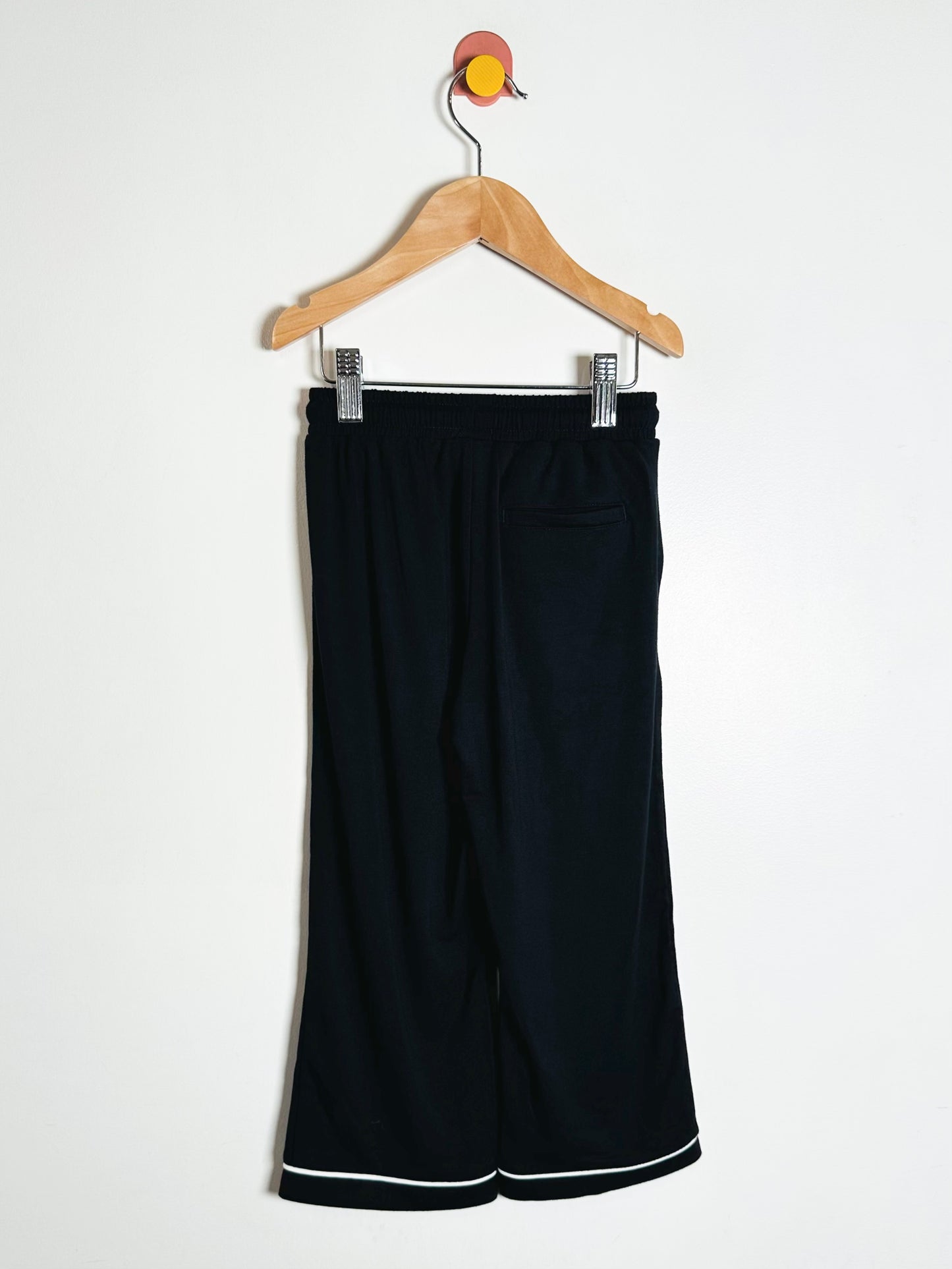 Black pants with white trim on a hanger against a white background