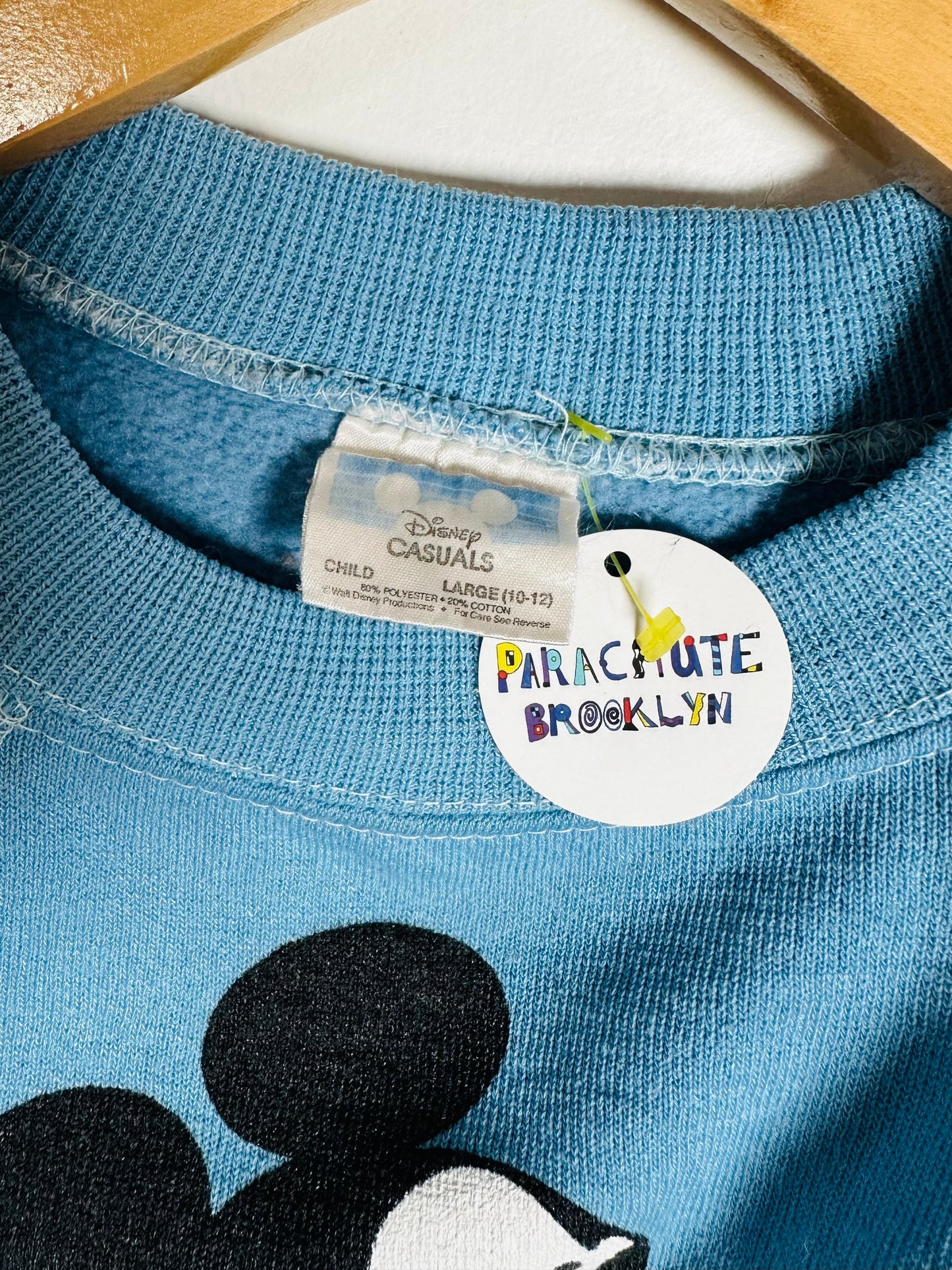 Blue shirt with a tag from Disney Casuals and Parachute Brooklyn on a wooden surface.