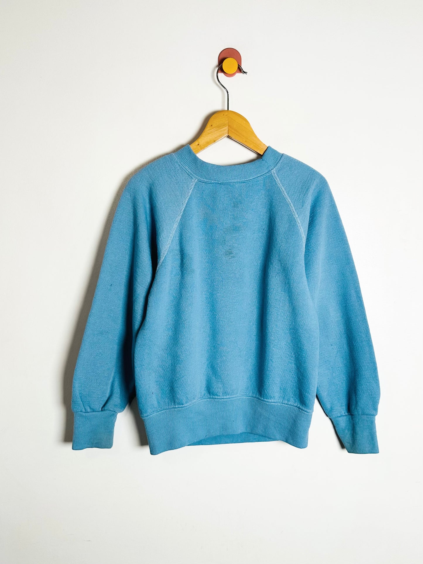 Blue sweatshirt on a wooden hanger against a white background