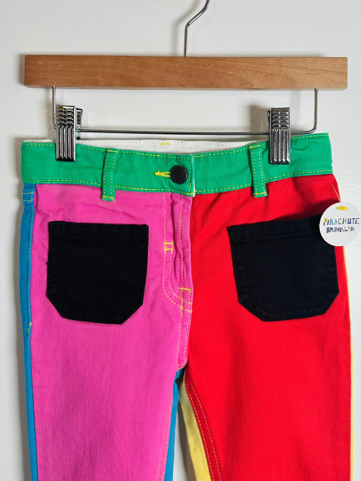 Colorful pants with green, pink, and red sections hanging on a wooden hanger.