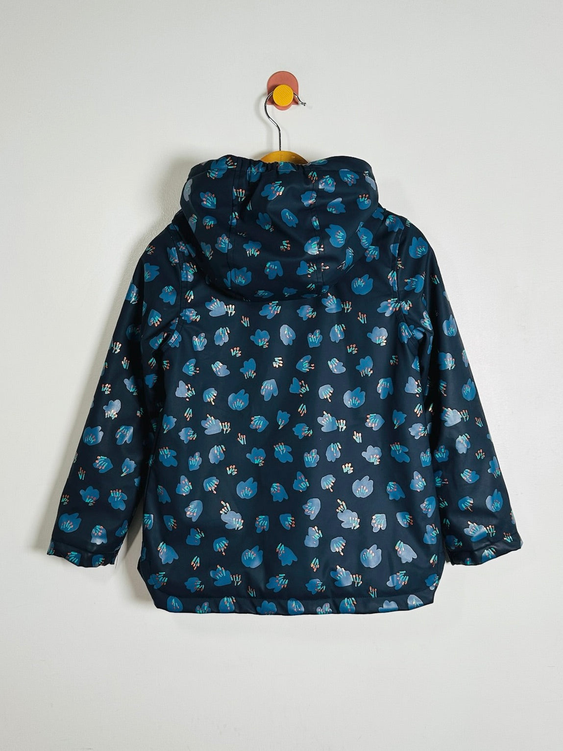 A hooded jacket with a dark navy blue base and an all-over blue and white floral pattern, hanging on a wooden hanger against a plain white wall.