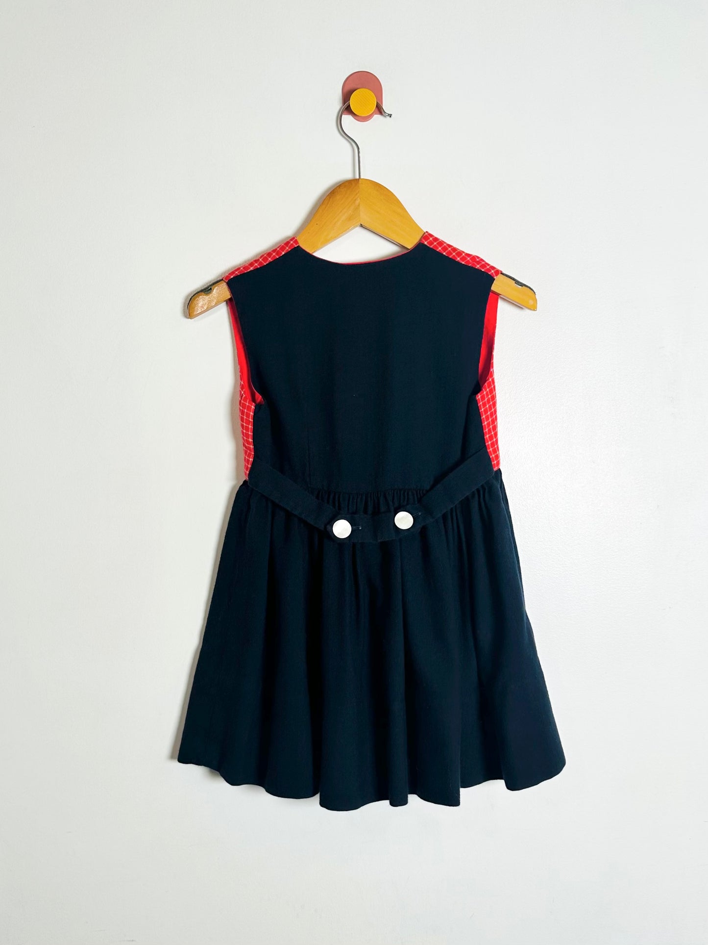 Navy blue dress with red accents on a wooden hanger against a white background
