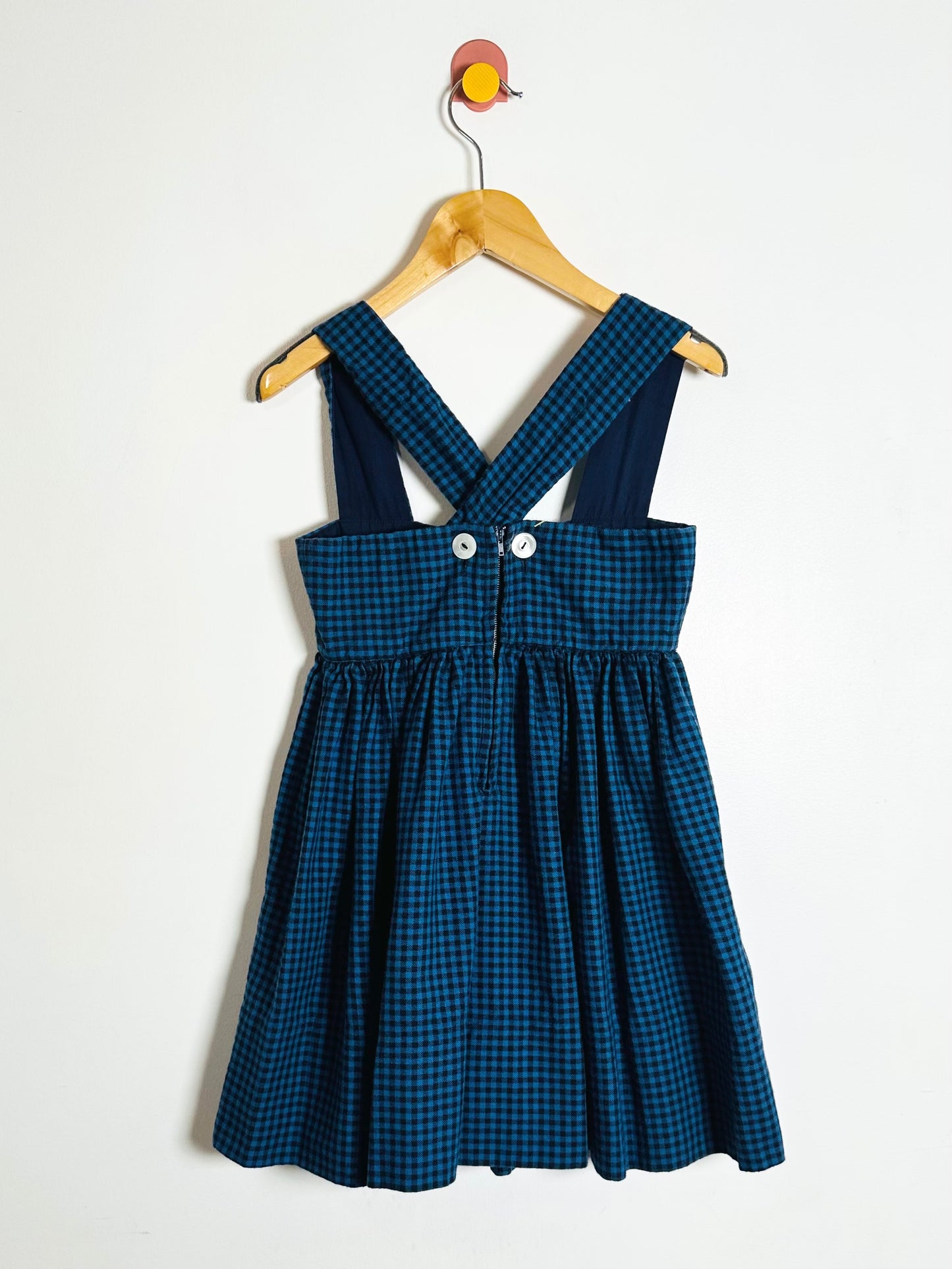 Blue checkered dress on a wooden hanger against a white background