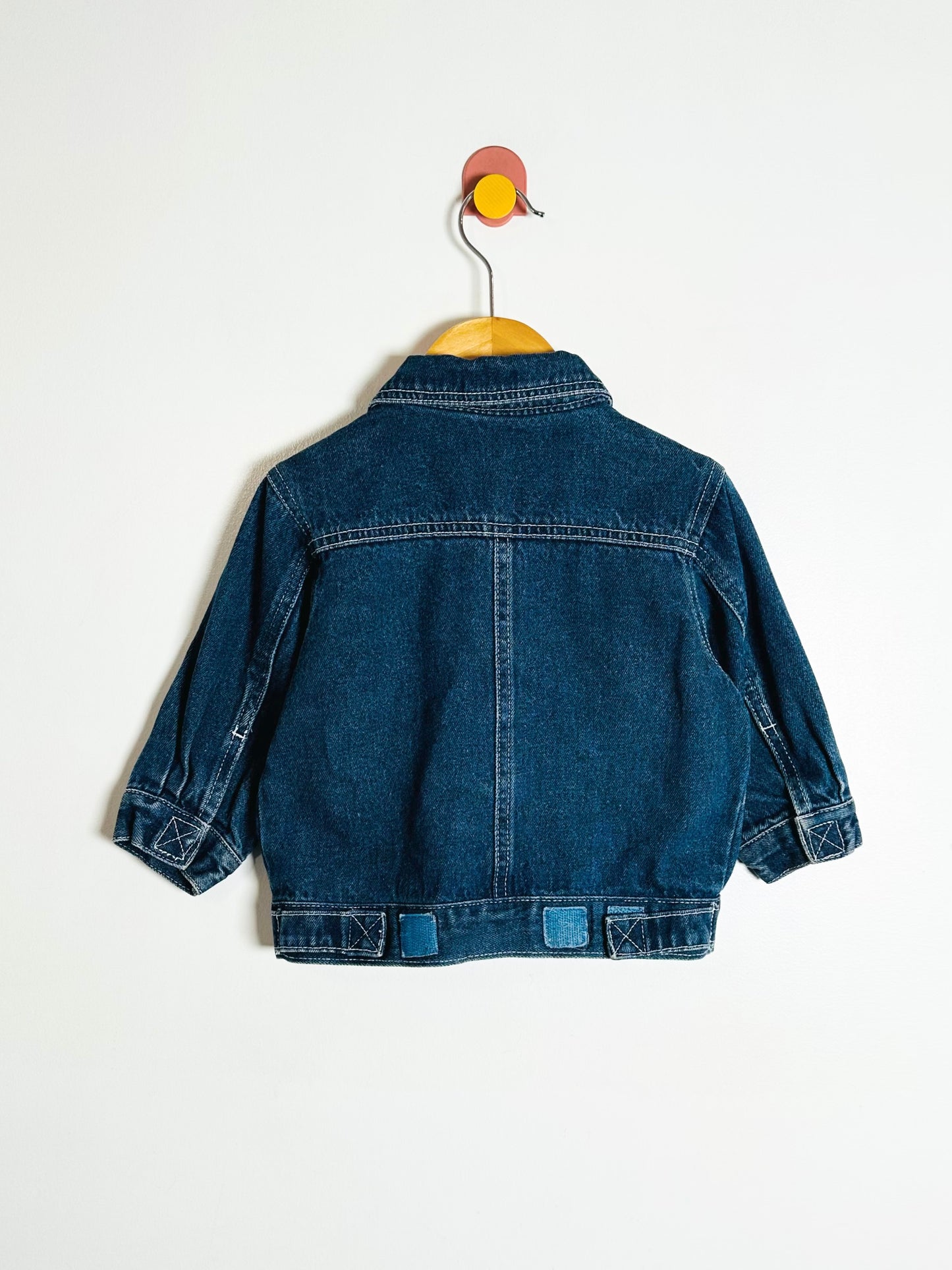 Blue denim jacket on a hanger against a white background