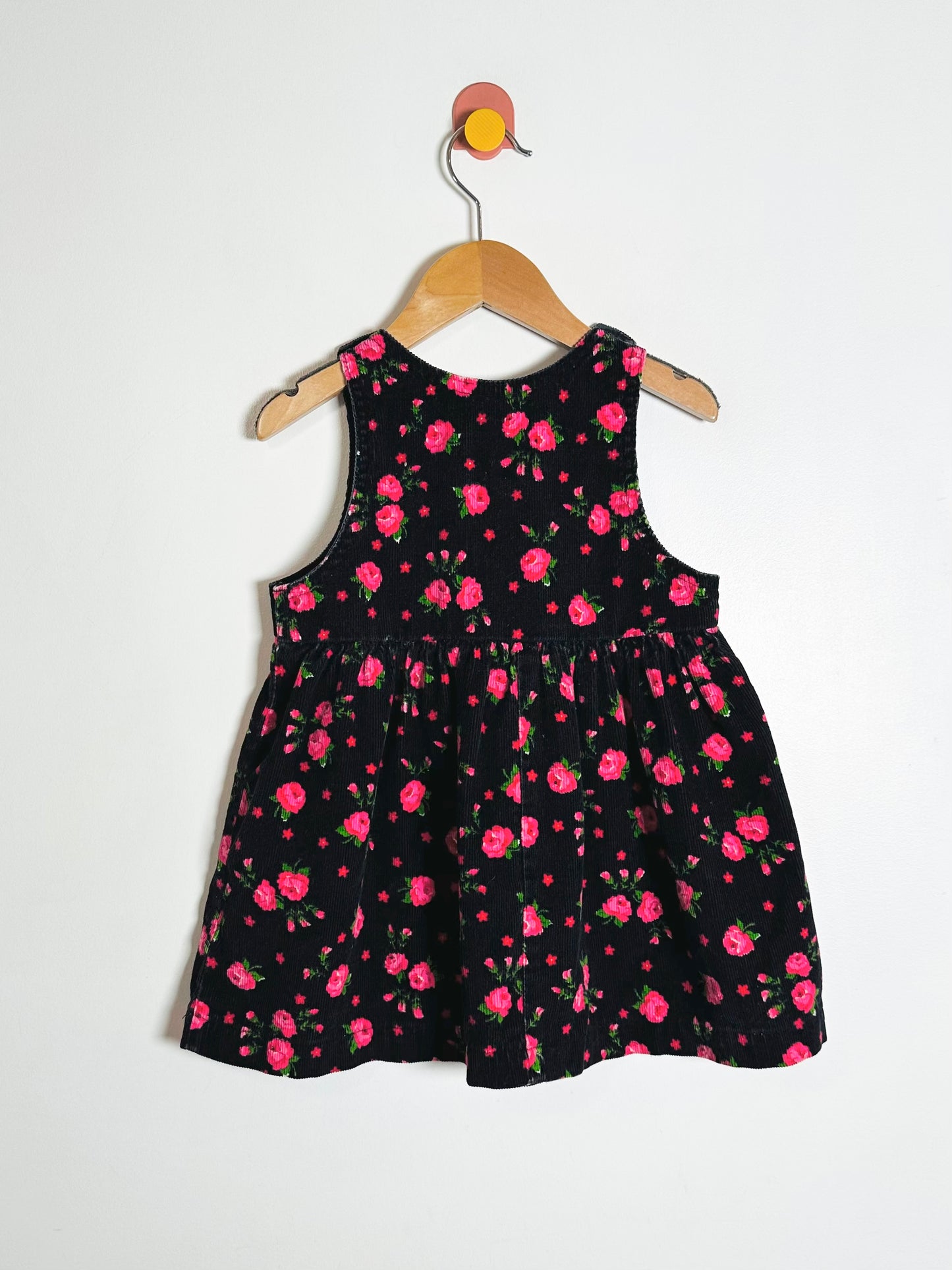 Black dress with pink floral pattern on a hanger against a white background