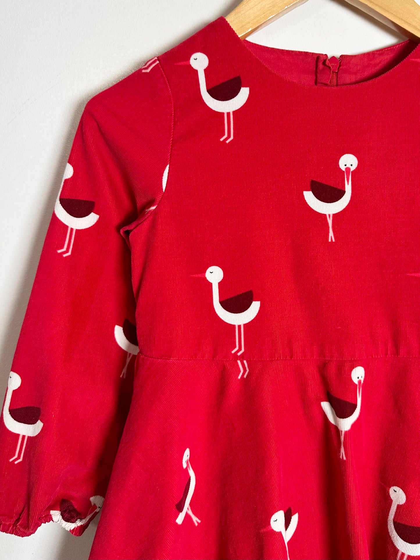 Red dress with white bird pattern on a hanger against a white background