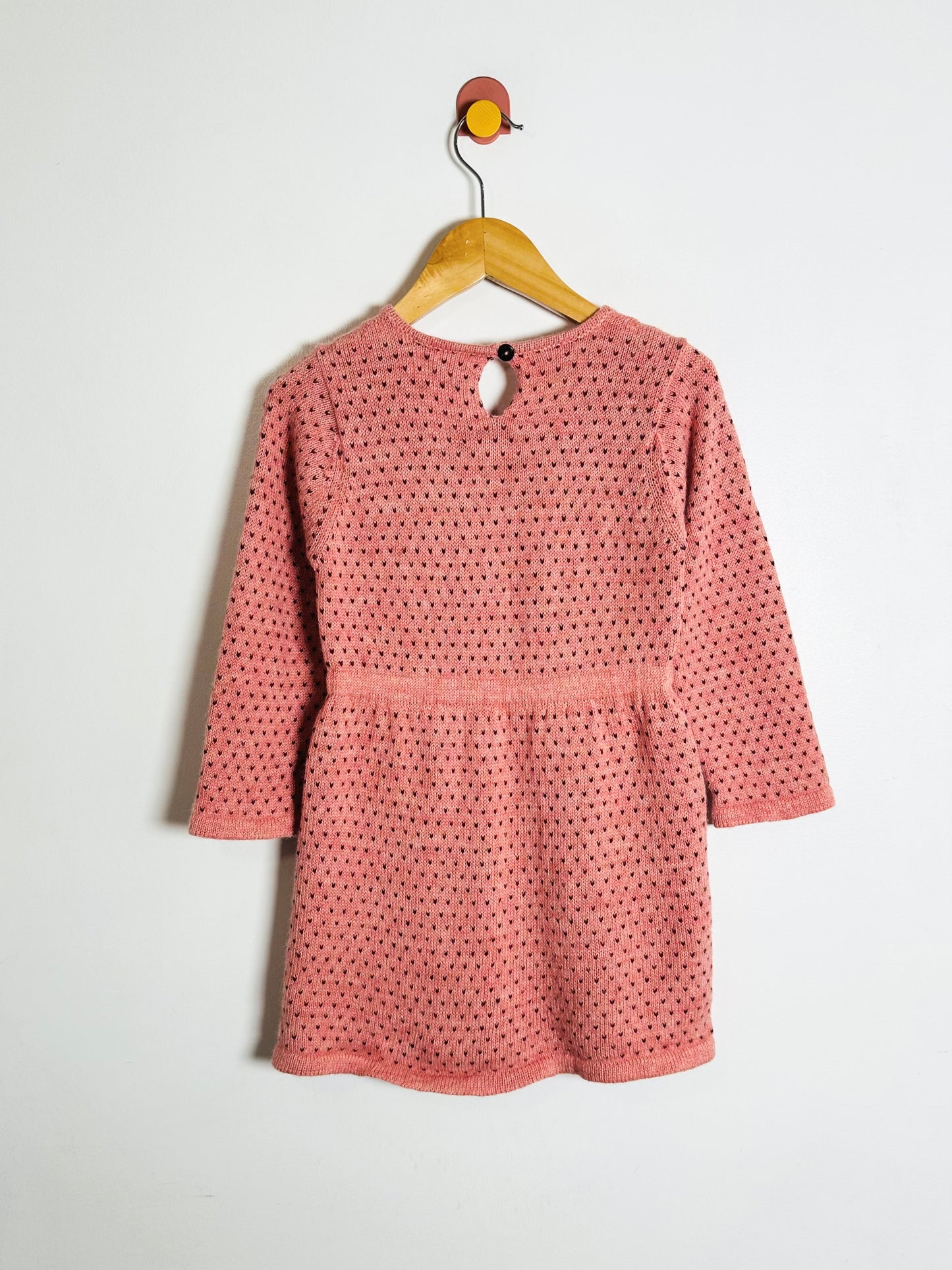Pink polka dot dress on a hanger against a white background