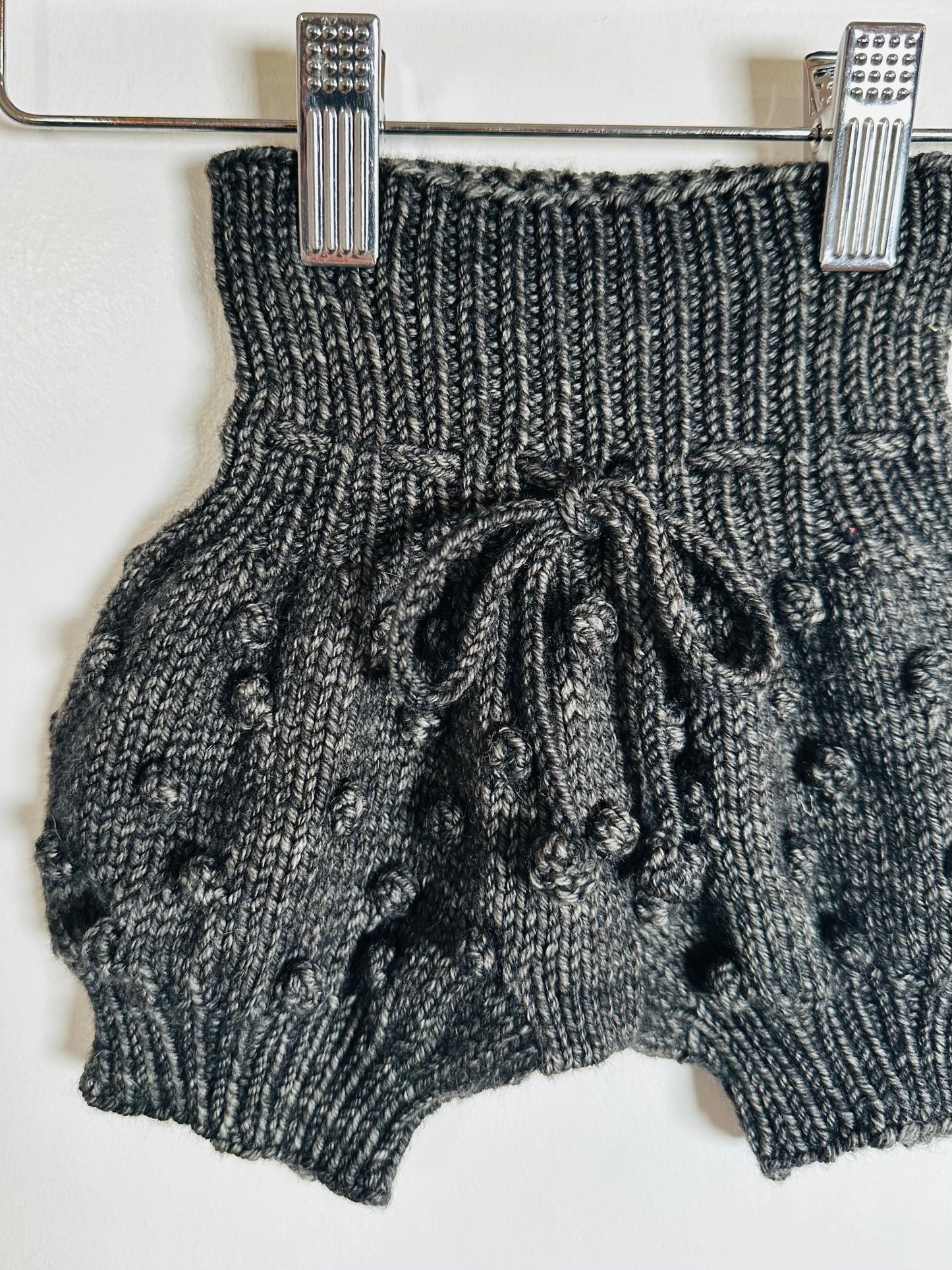 Knitted gray shorts with black polka dots hanging on a rack.