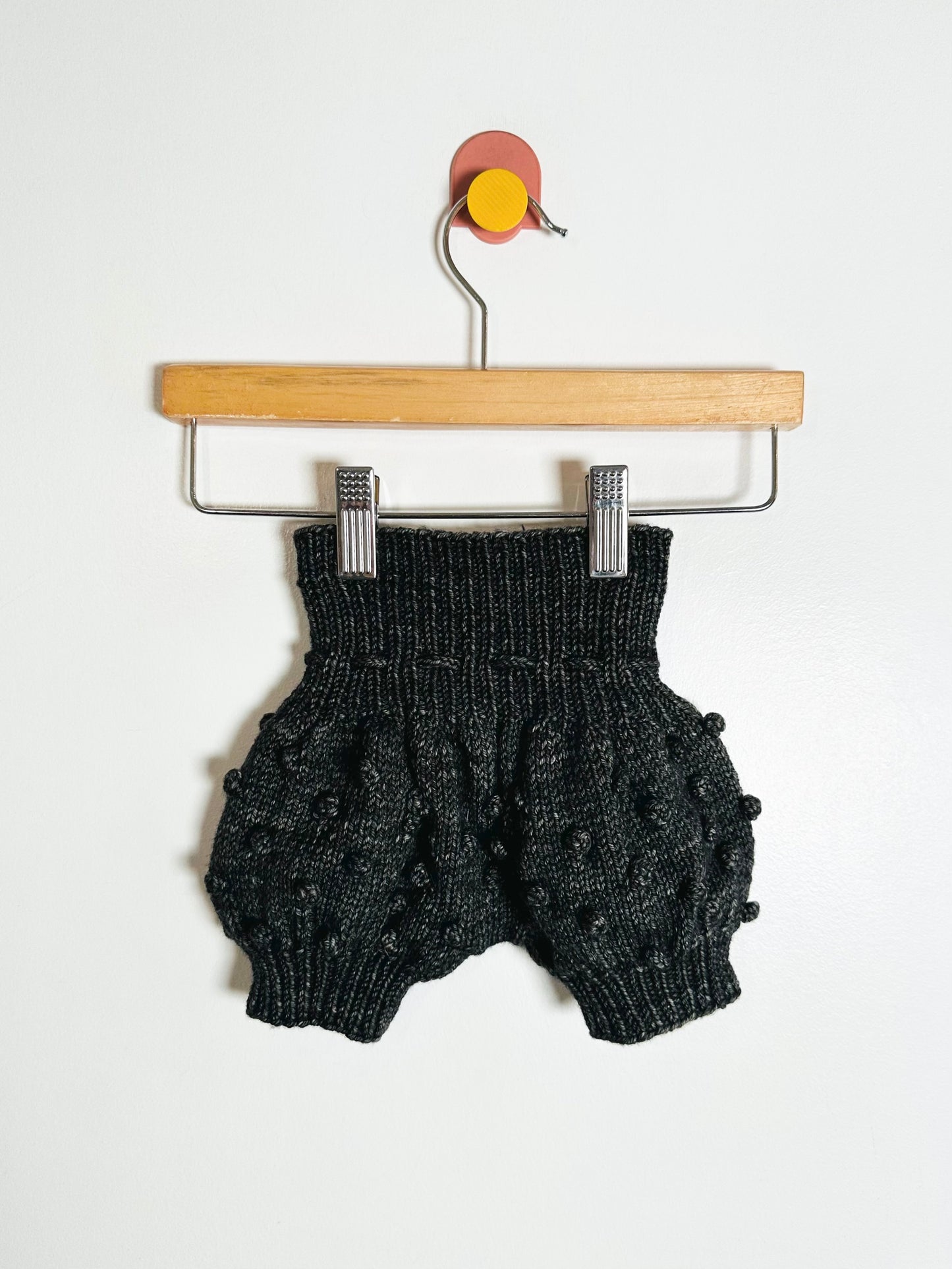 Black knitted baby romper on a hanger against a white background