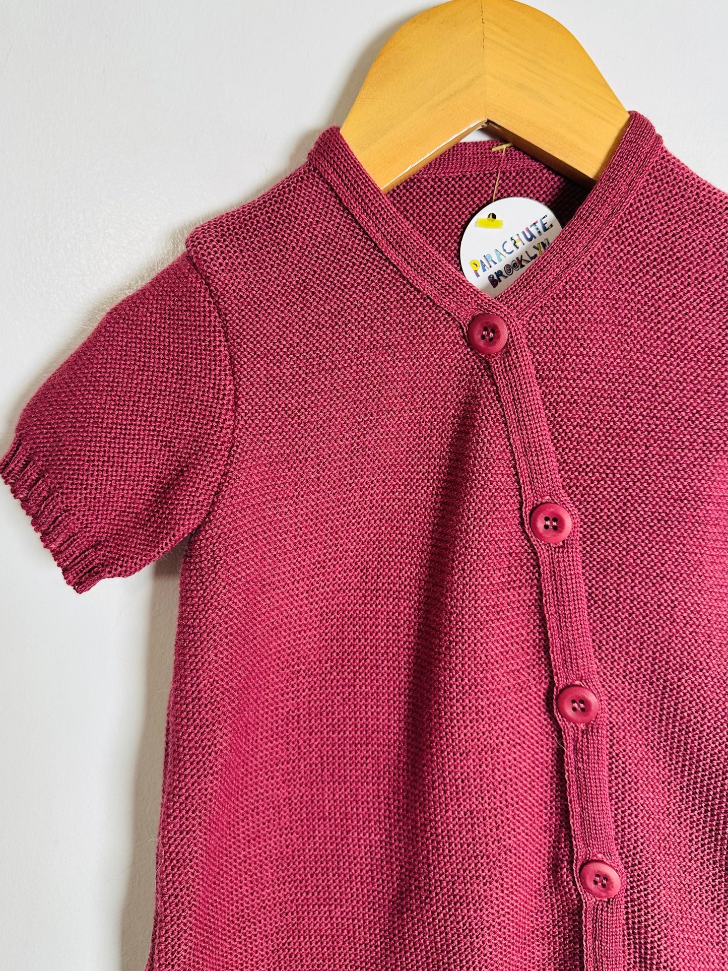 Pink knitted baby cardigan on a wooden hanger against a white background
