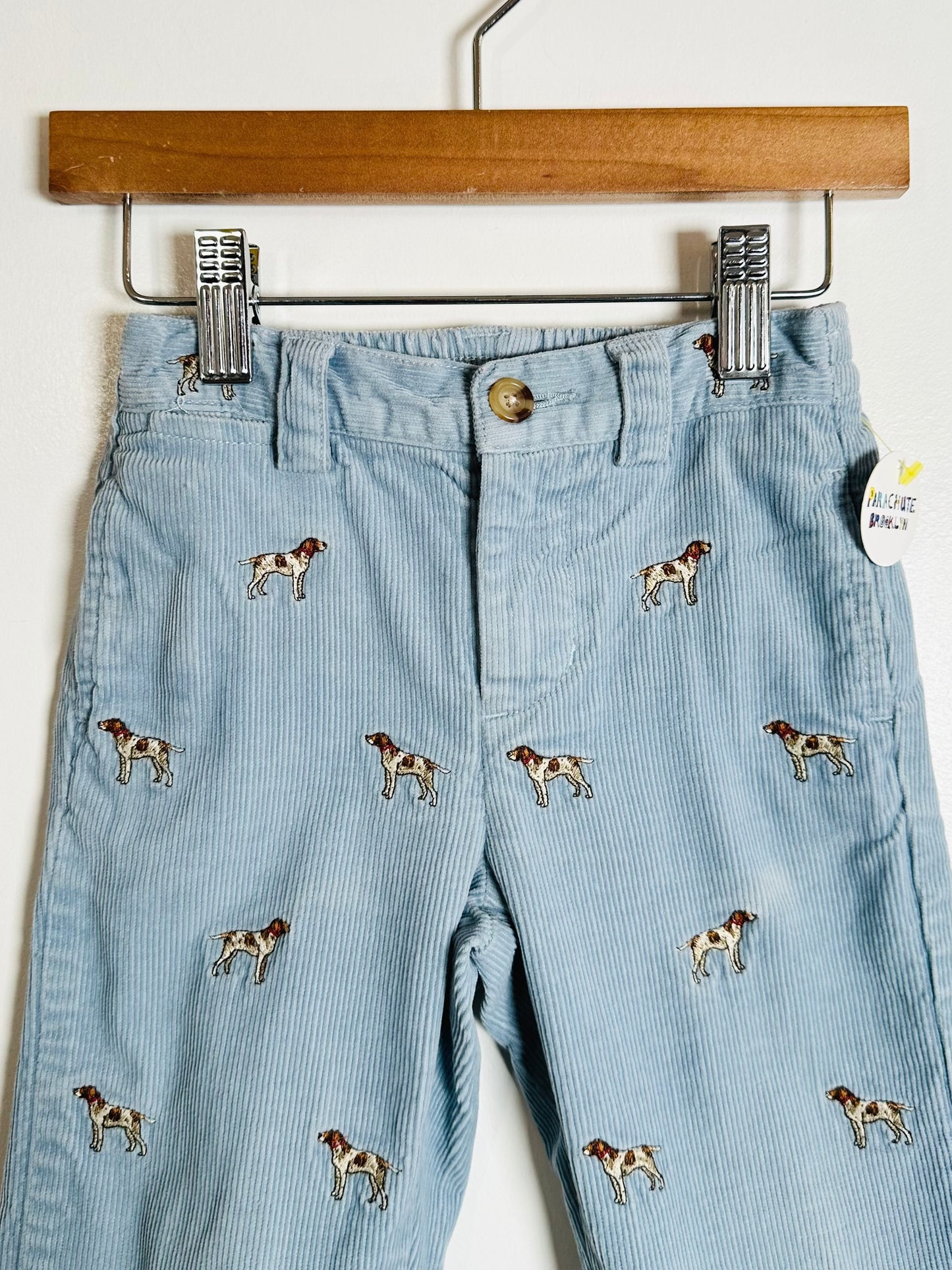 Light blue corduroy pants with dog pattern on a wooden hanger.
