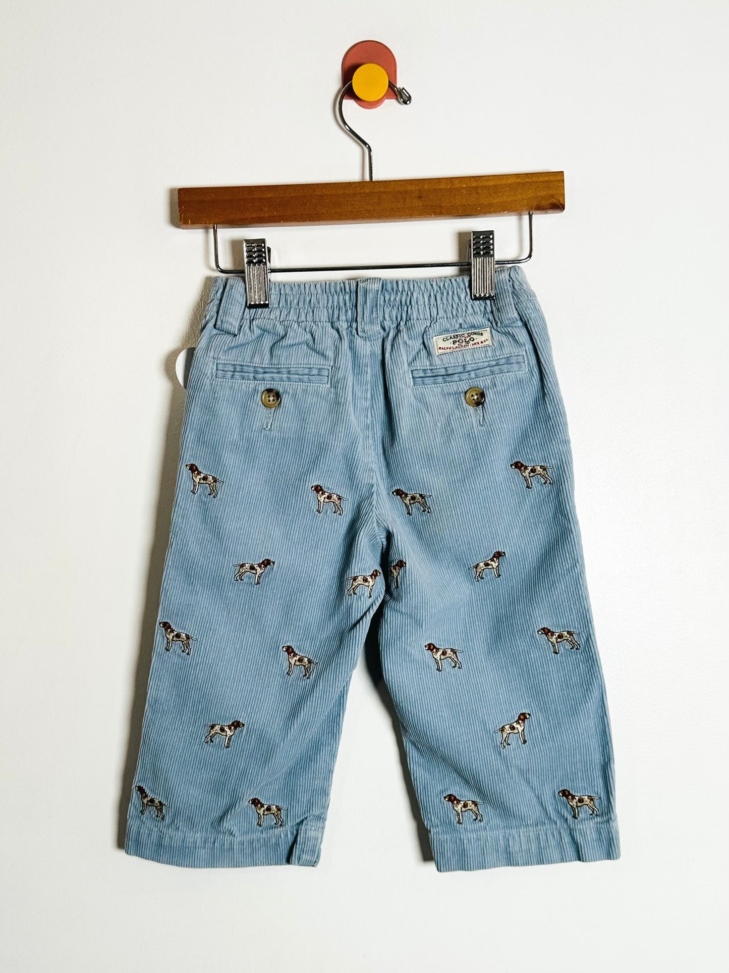 Light blue pants with dog pattern on a hanger against a white background
