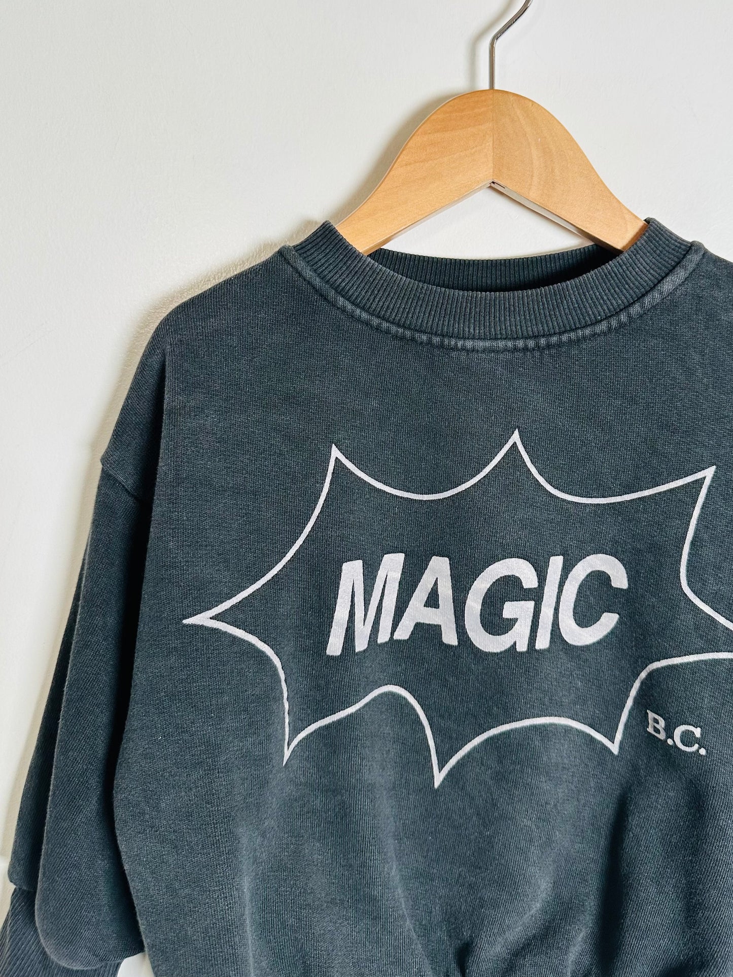 Gray sweatshirt with 'MAGIC B.C.' text on a hanger against a white background