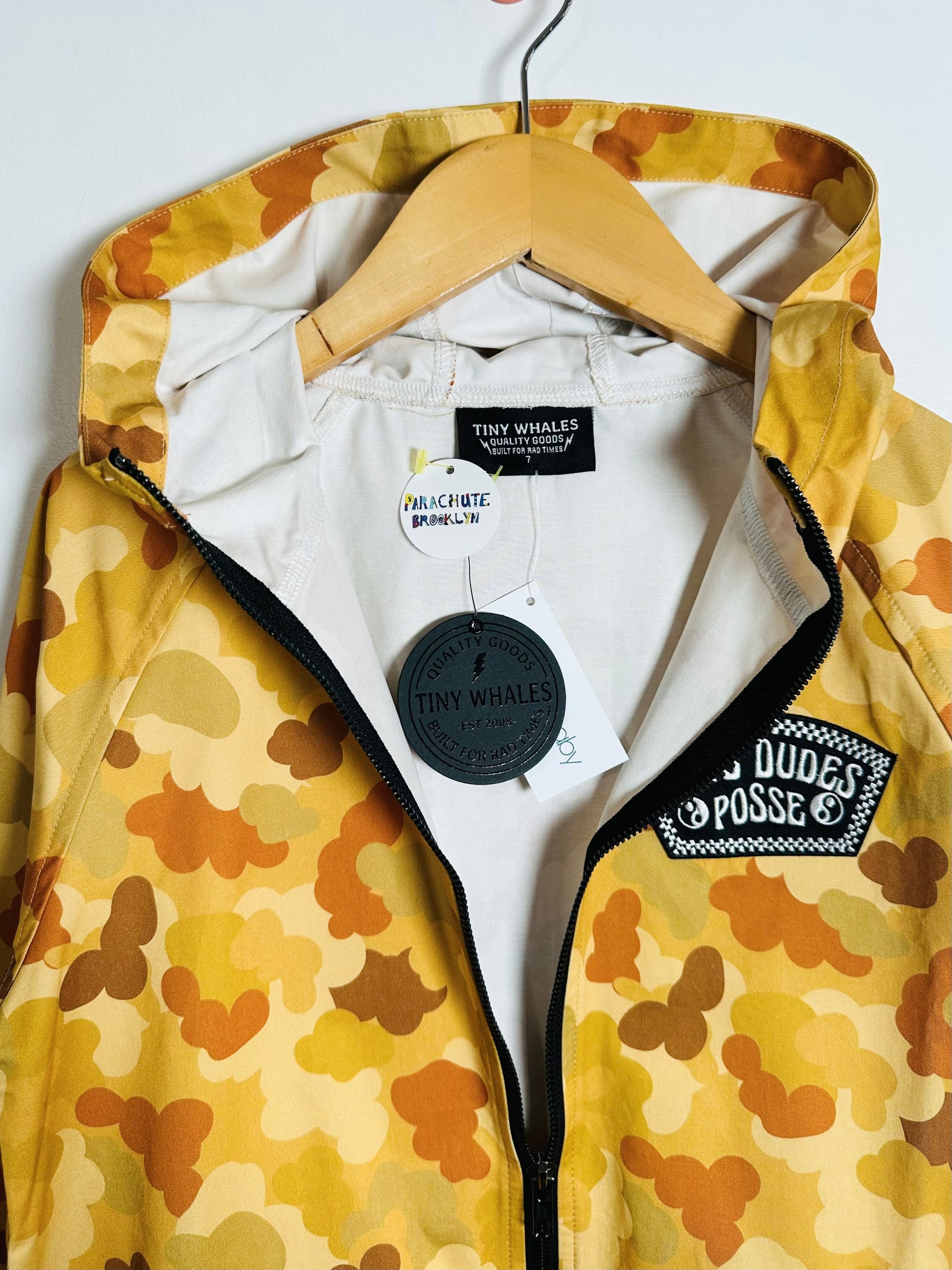 Yellow camouflage jacket with patches on a hanger against a white background