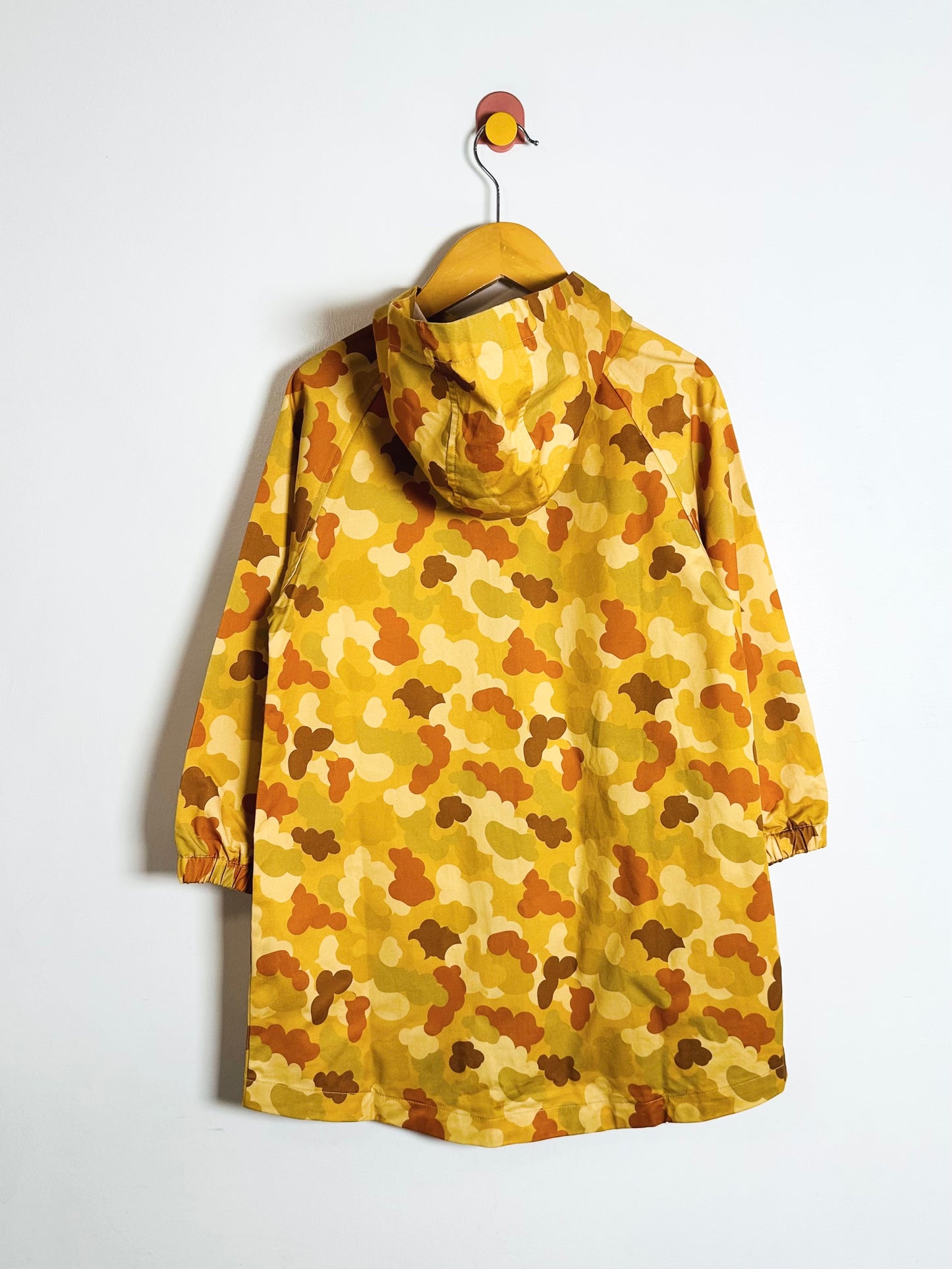 Yellow camouflage-patterned raincoat on a hanger against a white background