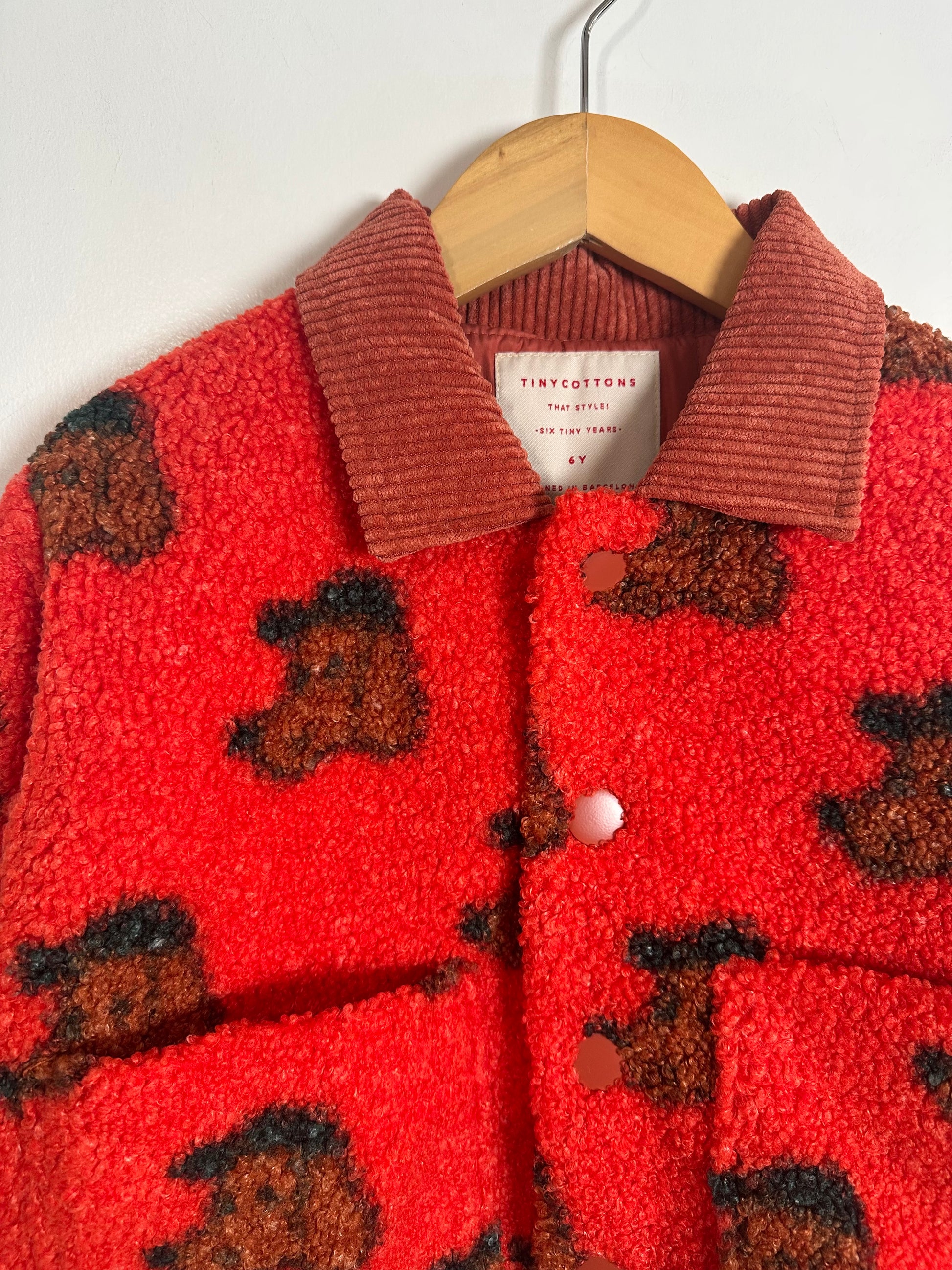 Red fleece jacket with brown dog pattern on a hanger against a white background
