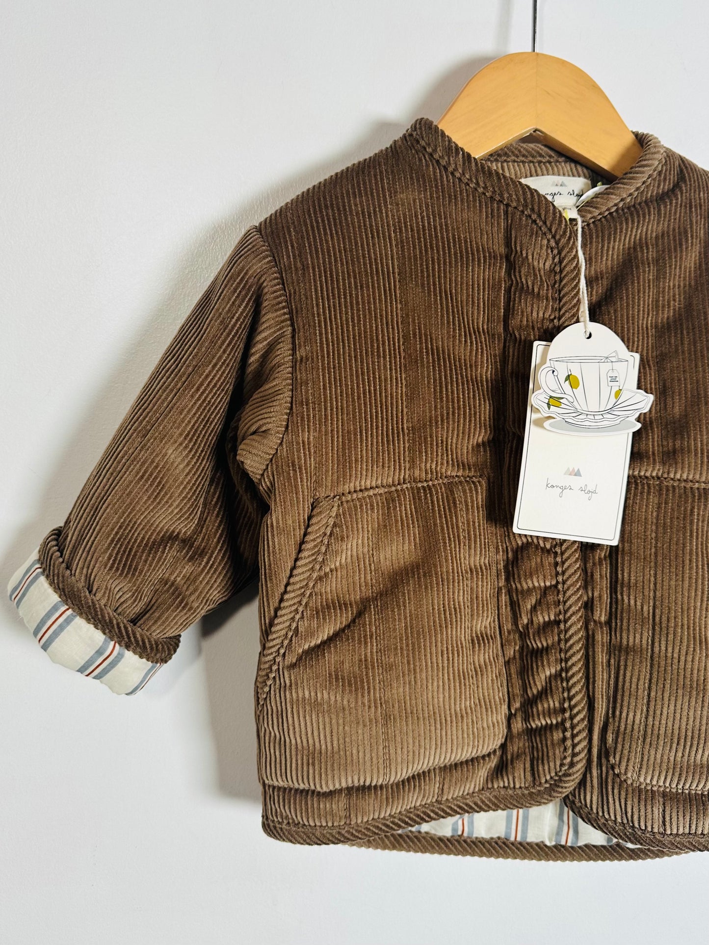 Brown corduroy jacket on a hanger with a tag against a white background