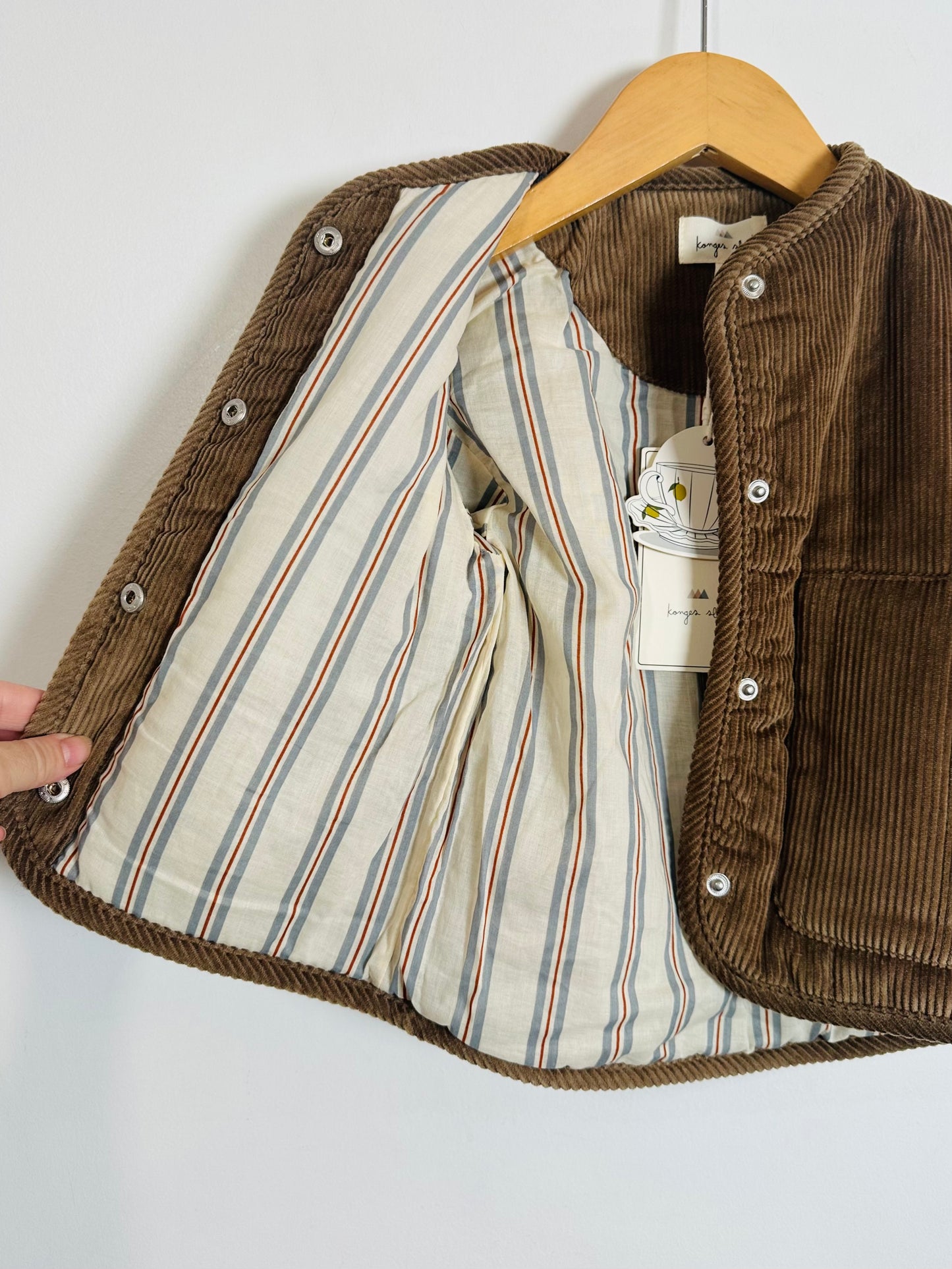Brown corduroy jacket with striped lining on a hanger against a white background
