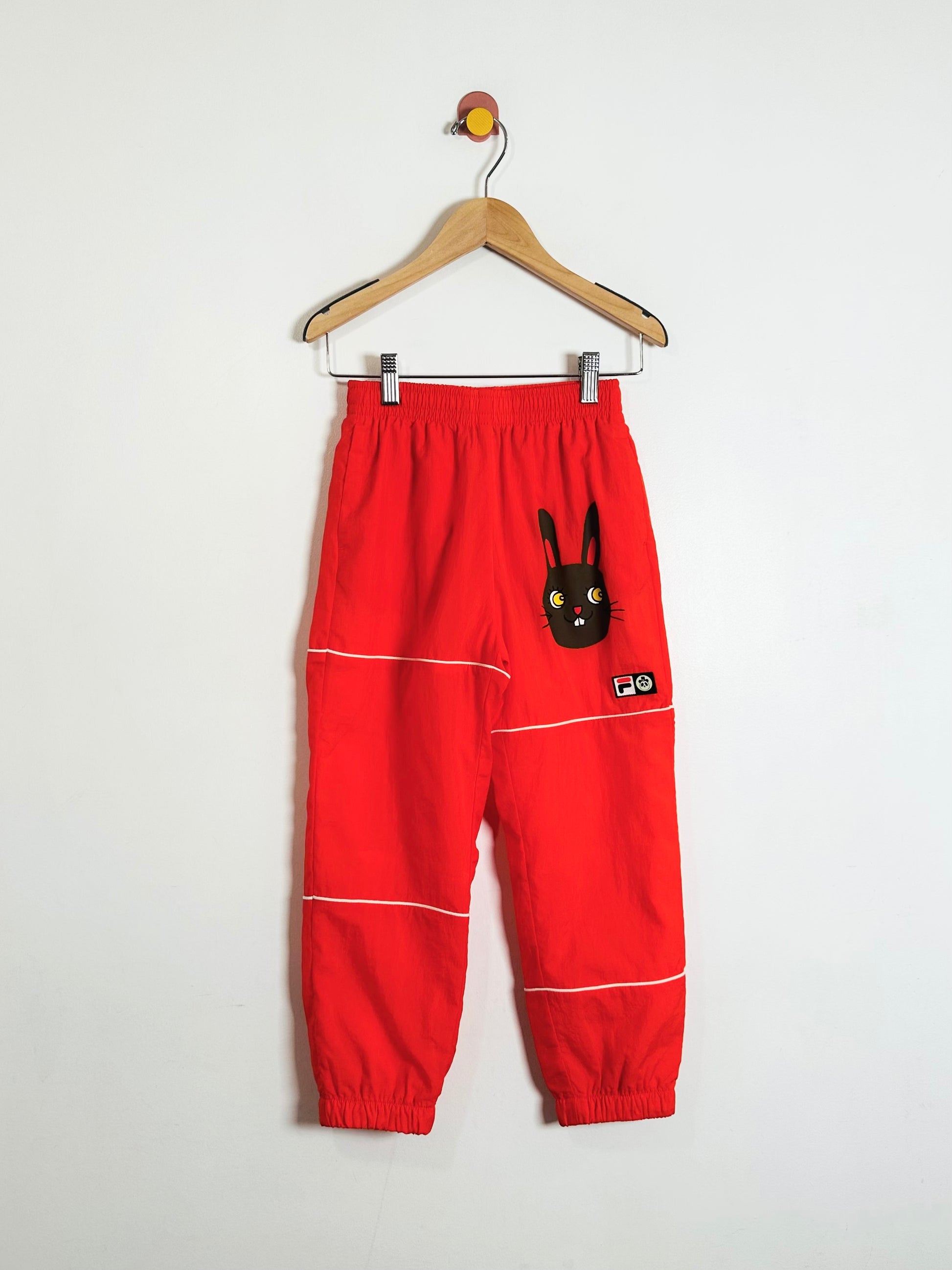 Red pants with a bunny design on a hanger against a white background