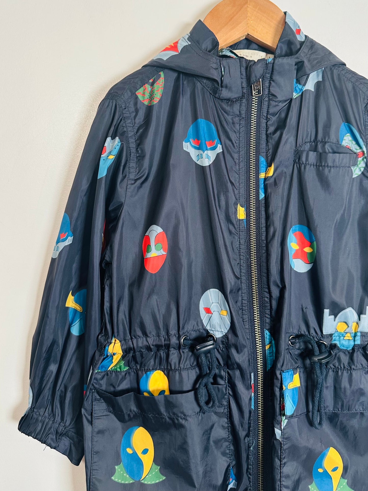 Children's navy jacket with colorful space-themed designs on a wooden hanger against a white background