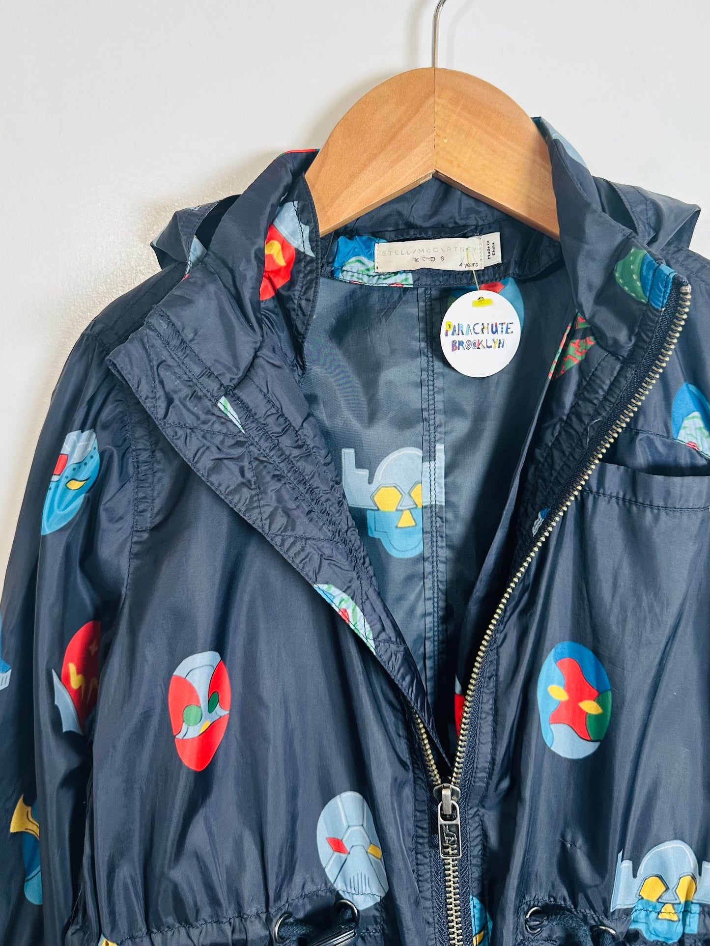Children's navy jacket with colorful space-themed designs on a wooden hanger against a white background.