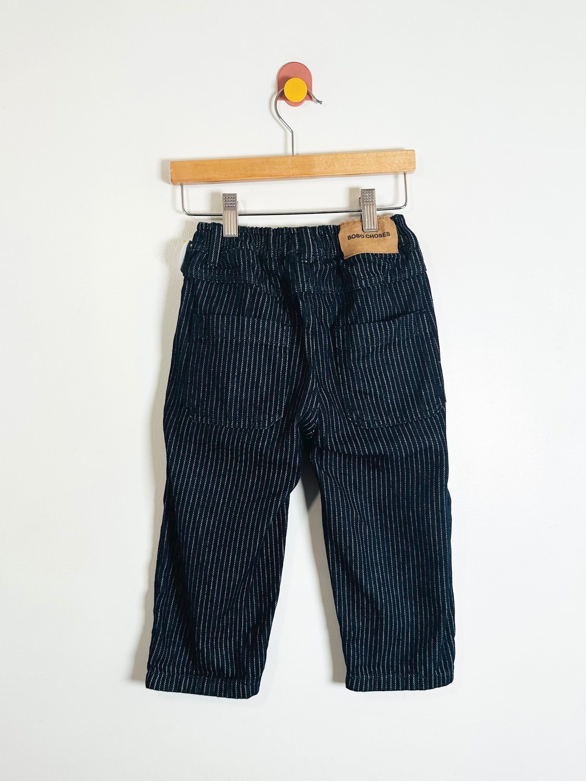Pair of dark blue striped pants on a wooden hanger against a white background