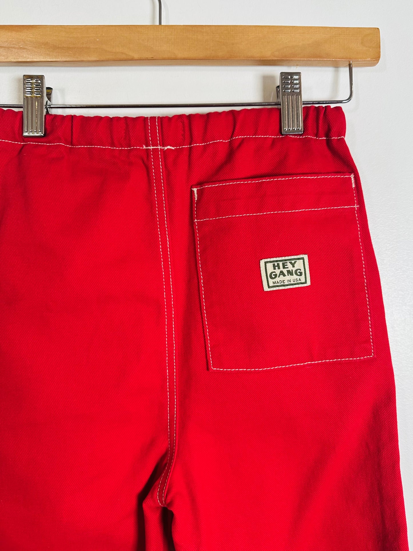 Red pants with a 'Hey Gang' logo on a hanger against a white background