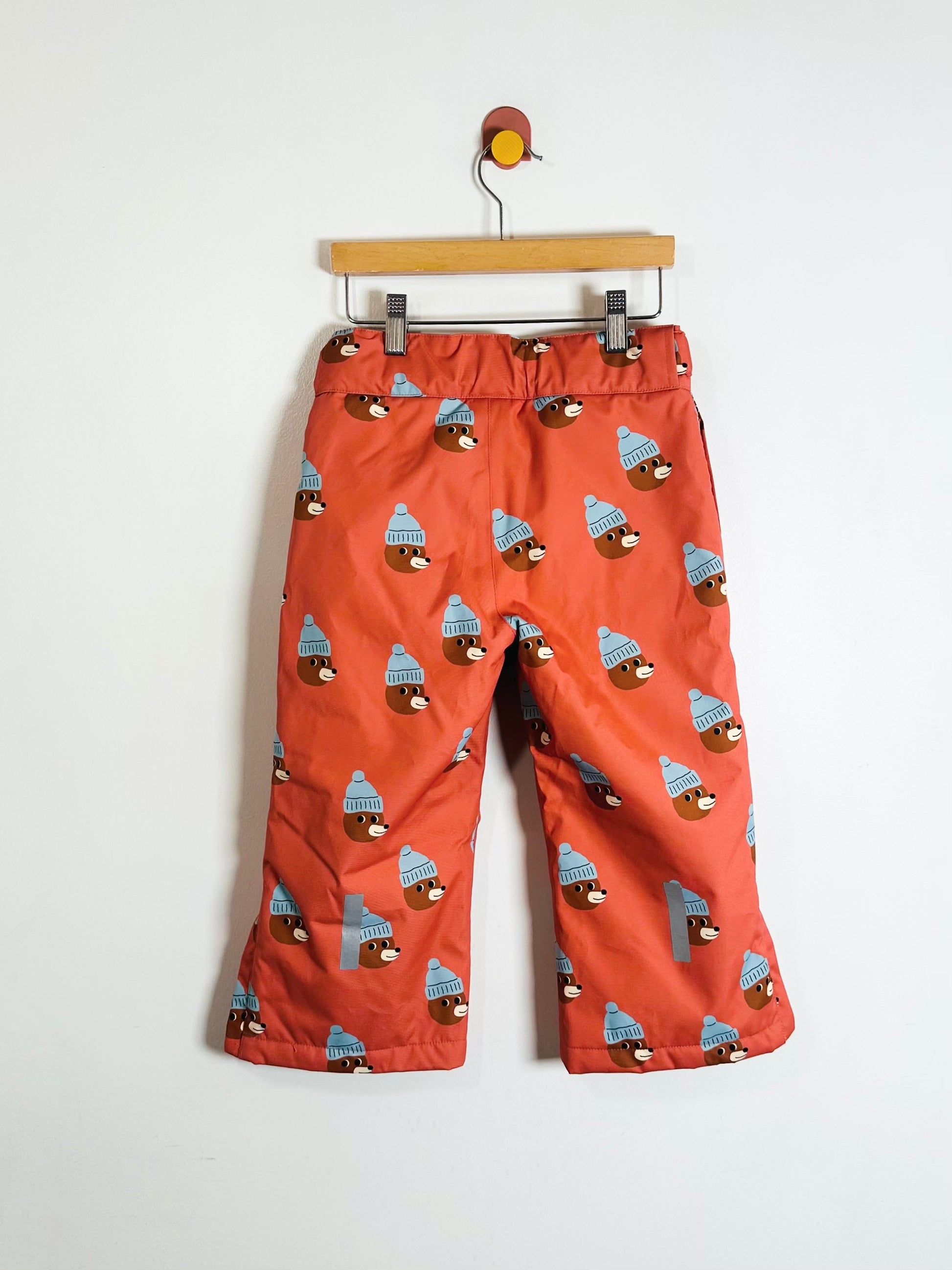 Children's orange pants with a pattern of dogs wearing hats on a hanger against a white background
